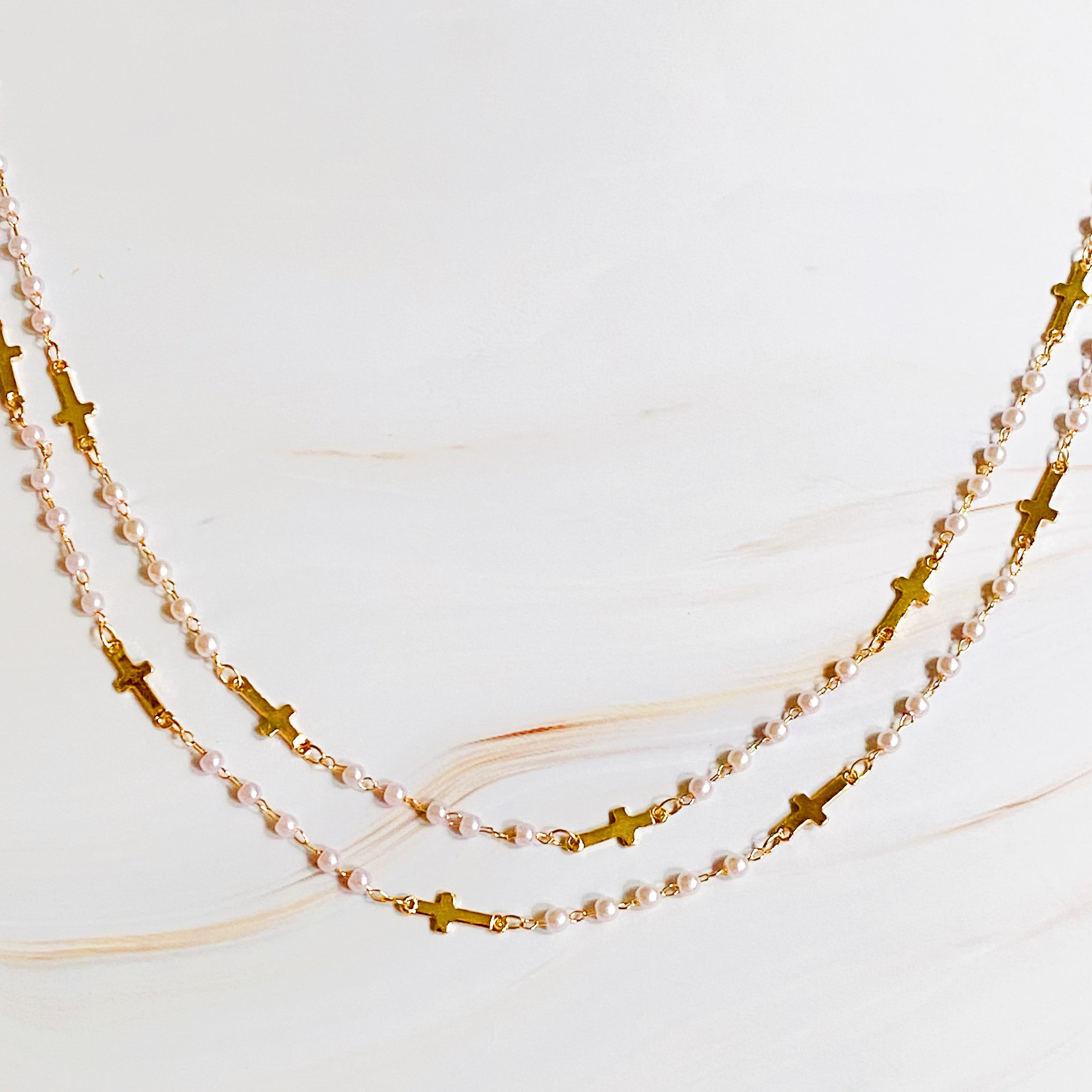 A stylish Pearls And Crosses Long Necklace featuring golden crosses and pearl beads, showcasing its elegant design and versatility.