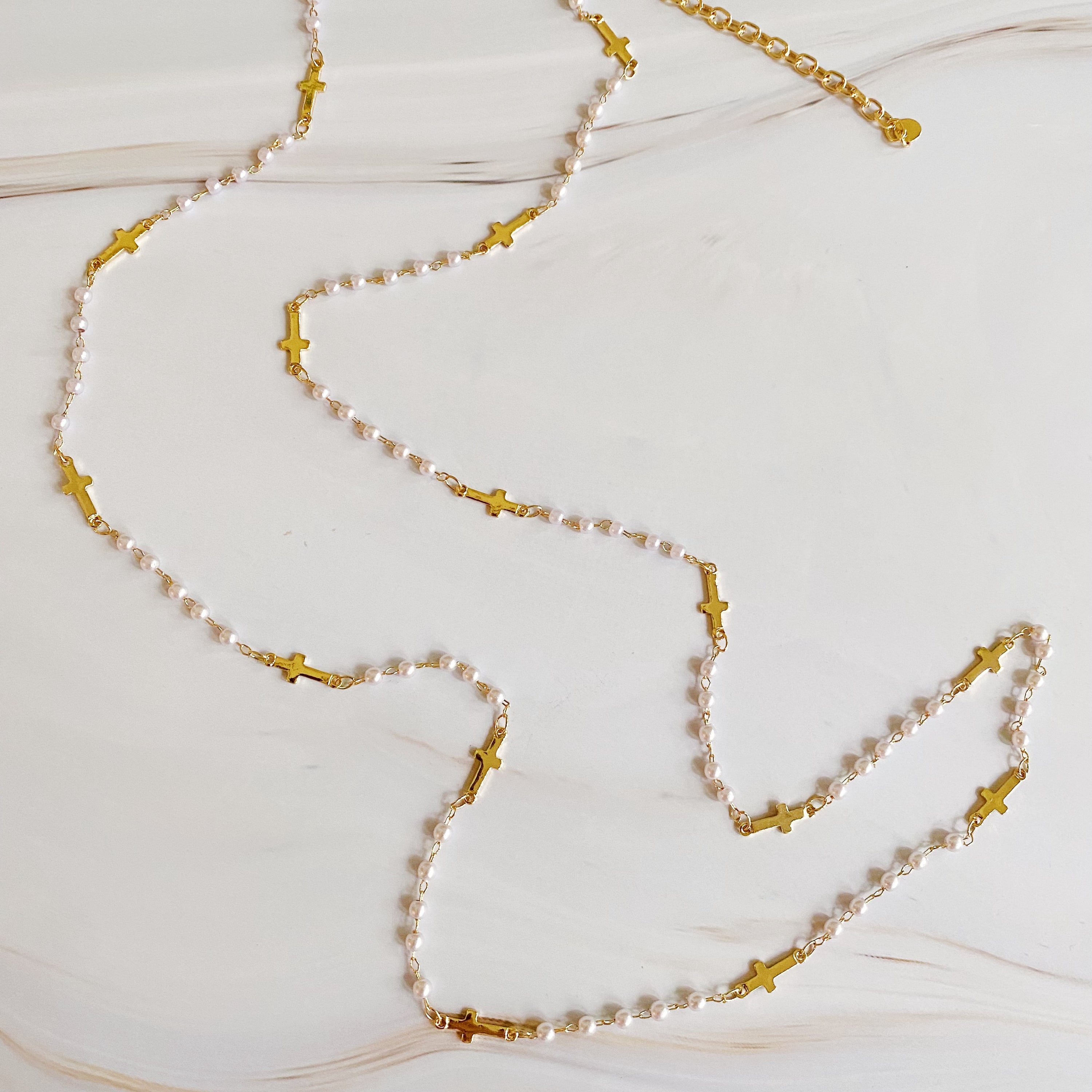 A stylish Pearls And Crosses Long Necklace featuring golden crosses and pearl beads, showcasing its elegant design and versatility.