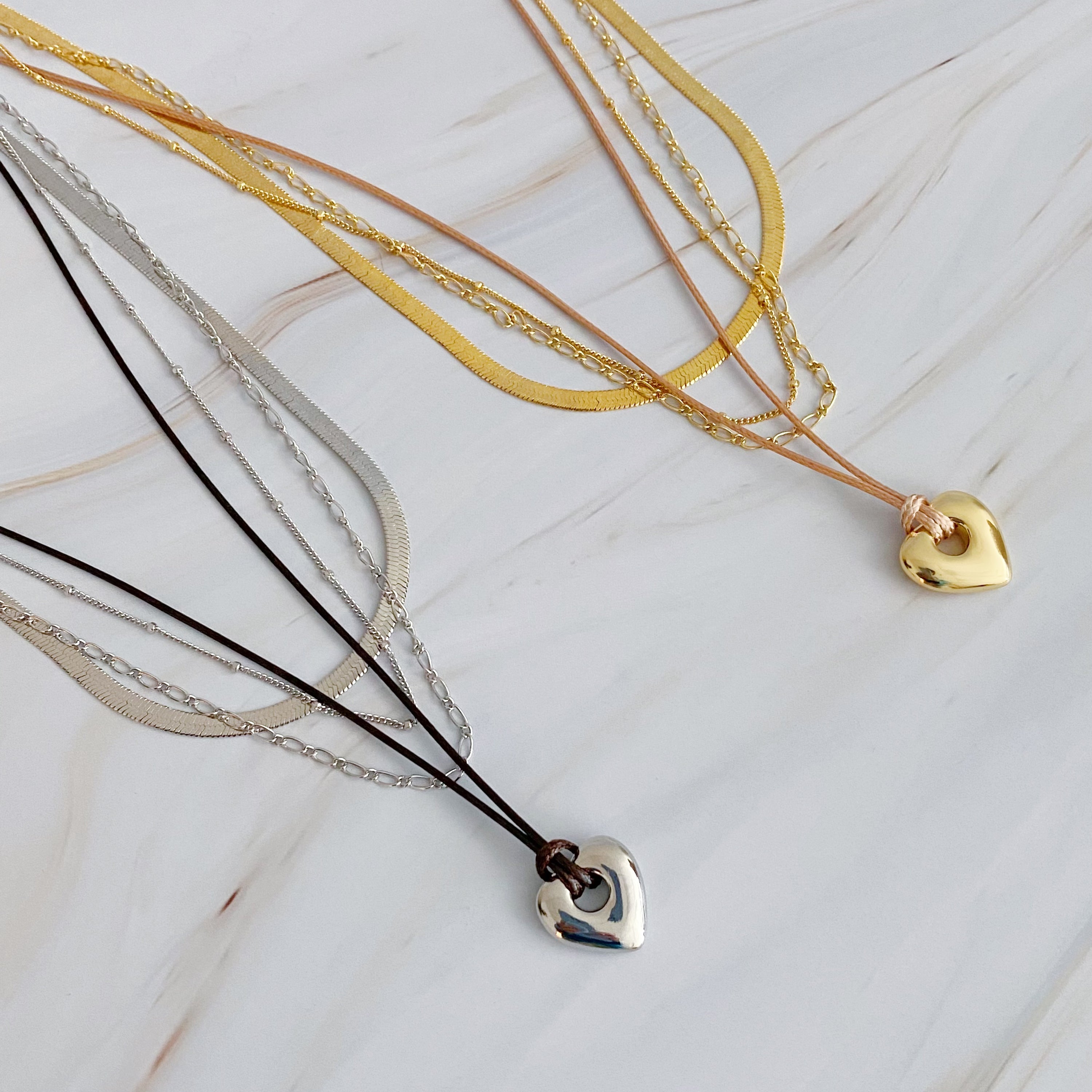 A beautifully layered heart and chain necklace featuring four strands, with a heart pendant and dainty metal chains in 18K gold plating.