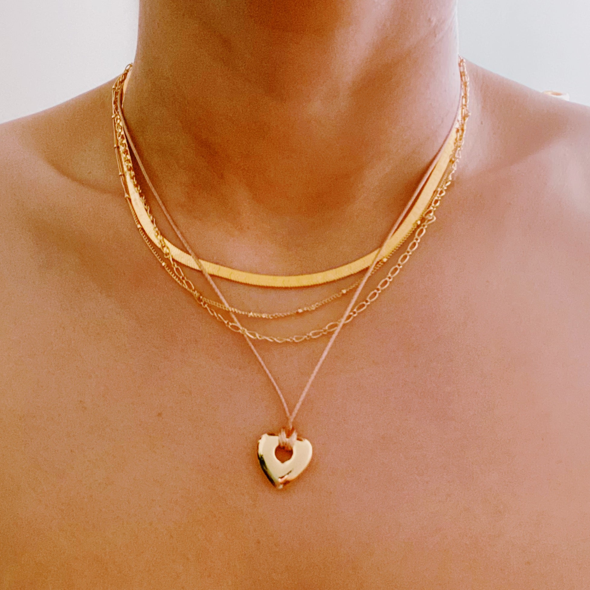 A beautifully layered heart and chain necklace featuring four strands, with a heart pendant and dainty metal chains in 18K gold plating.