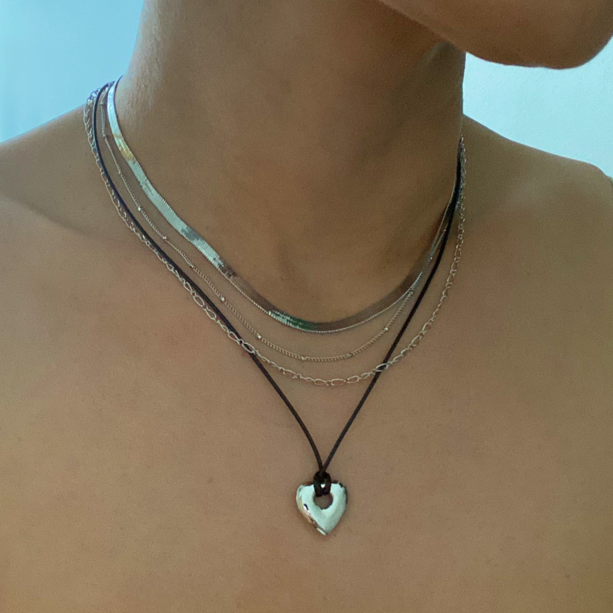 A beautifully layered heart and chain necklace featuring four strands, with a heart pendant and dainty metal chains in 18K gold plating.