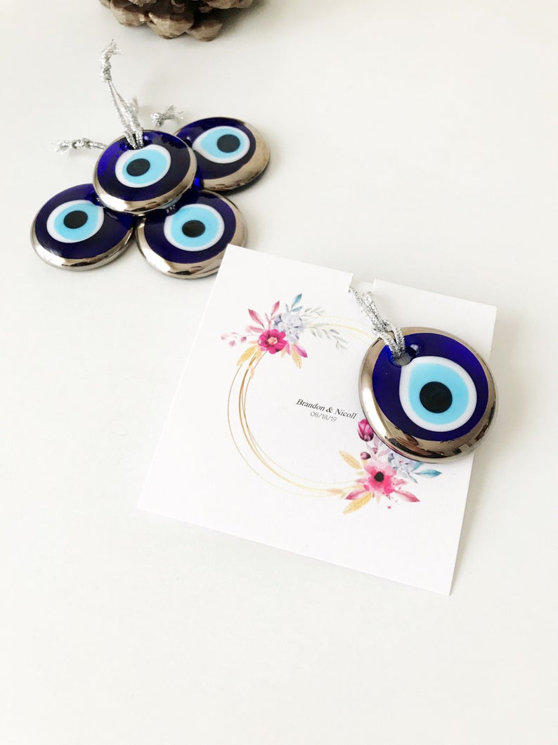 A collection of 50 personalized evil eye wedding gifts featuring gold, silver, and blue beads, beautifully arranged with custom cards.