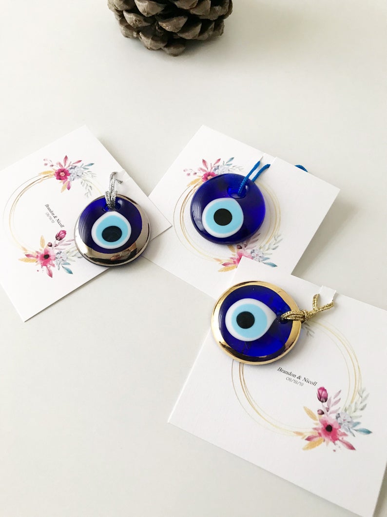 A collection of 50 personalized evil eye wedding gifts featuring gold, silver, and blue beads, beautifully arranged with custom cards.