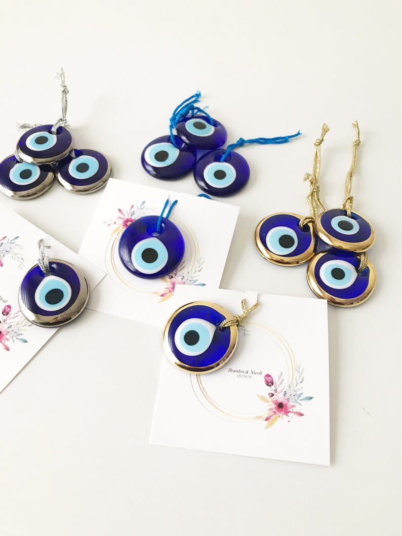 A collection of 50 personalized evil eye wedding gifts featuring gold, silver, and blue beads, beautifully arranged with custom cards.