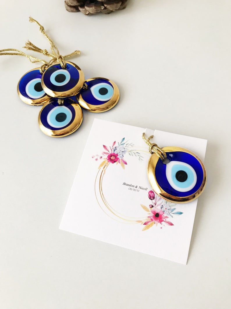 A collection of 50 personalized evil eye wedding gifts featuring gold, silver, and blue beads, beautifully arranged with custom cards.