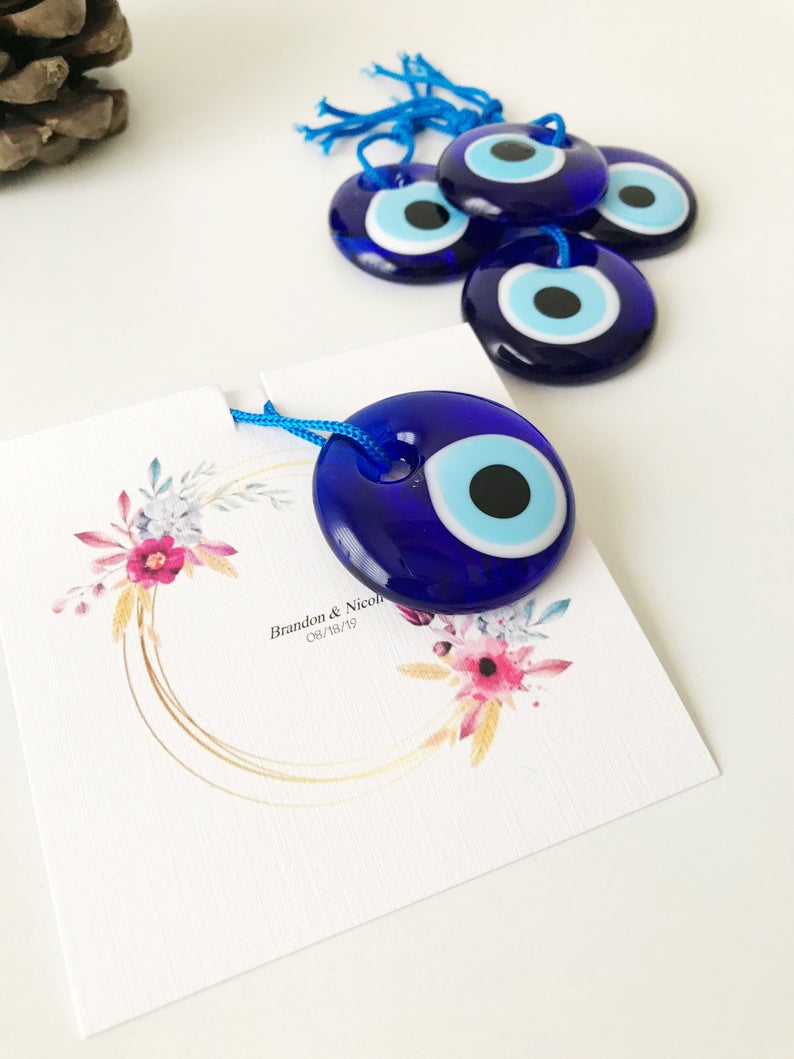 A collection of 50 personalized evil eye wedding gifts featuring gold, silver, and blue beads, beautifully arranged with custom cards.