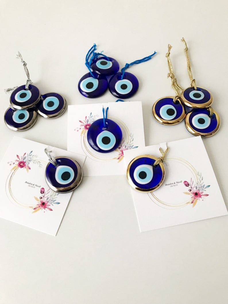 A collection of 50 personalized evil eye wedding gifts featuring gold, silver, and blue beads, beautifully arranged with custom cards.