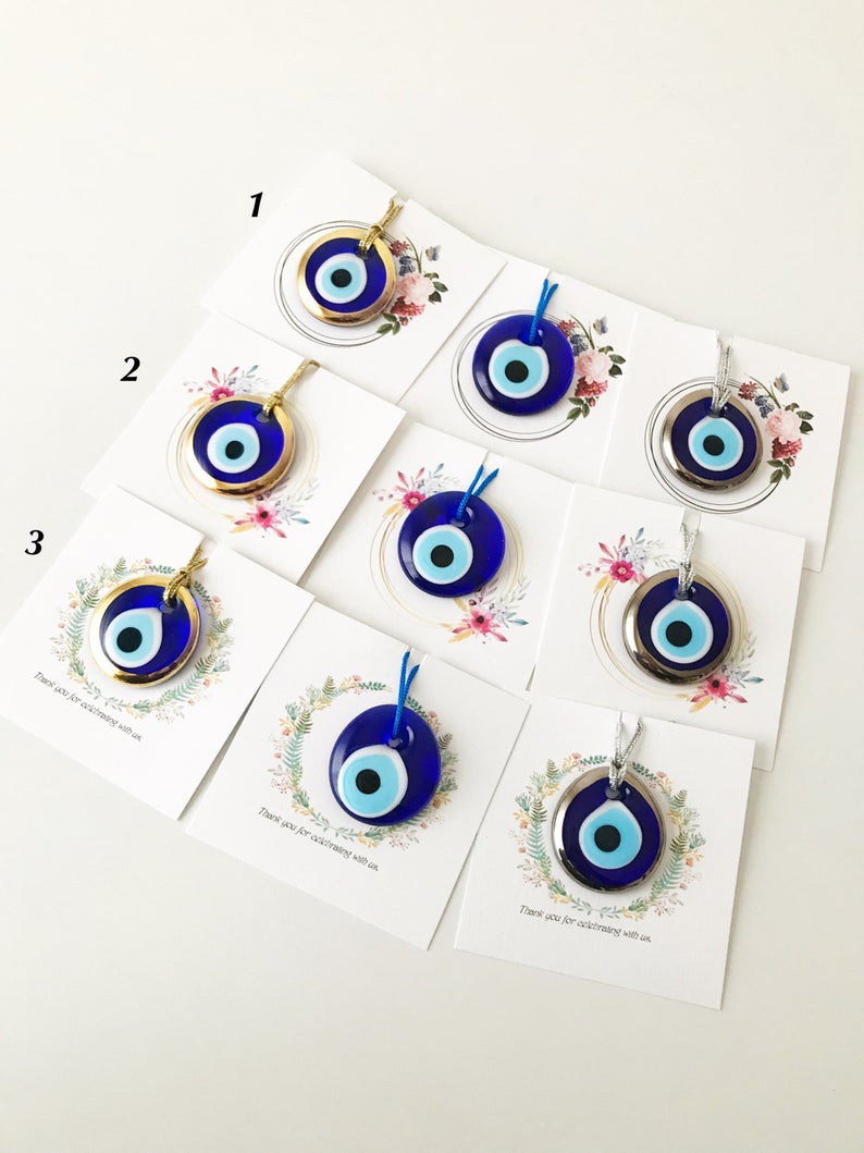 A collection of 10 handmade glass evil eye beads with personalized cards, featuring blue, gold, and silver colors, perfect for wedding favors.