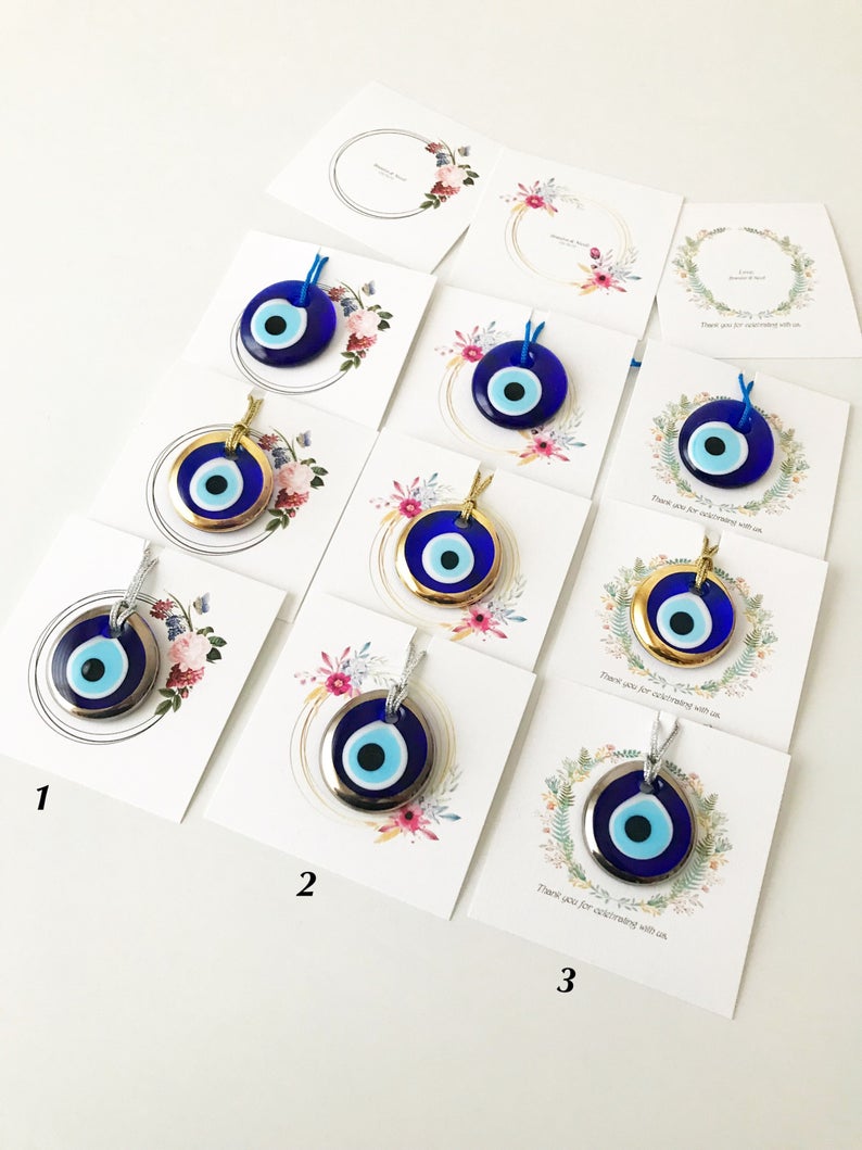 A collection of 10 handmade glass evil eye beads with personalized cards, featuring blue, gold, and silver colors, perfect for wedding favors.