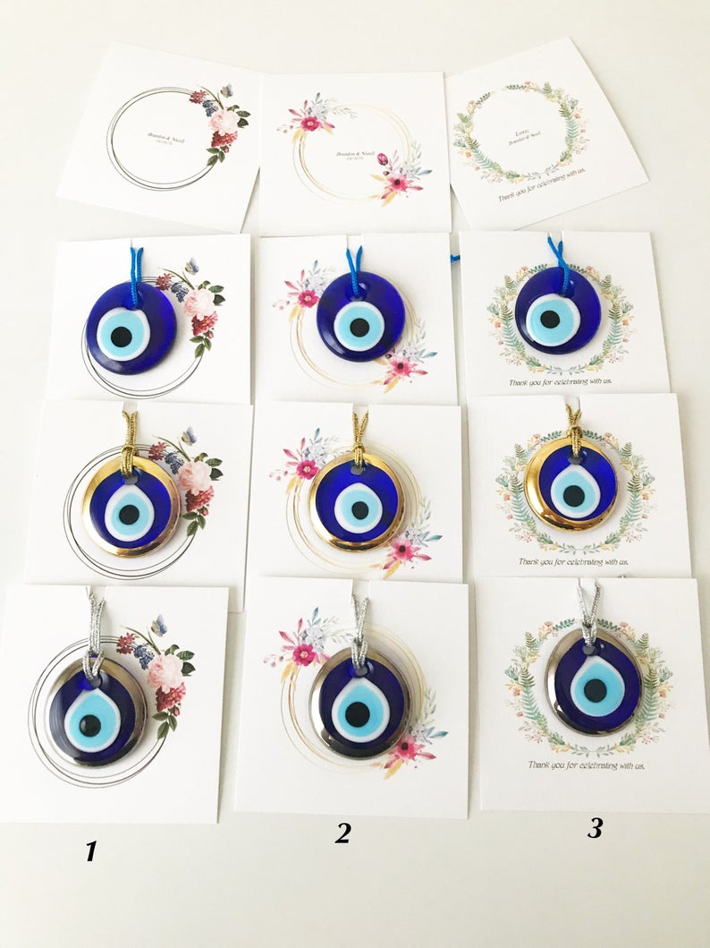 A collection of 10 handmade glass evil eye beads with personalized cards, featuring blue, gold, and silver colors, perfect for wedding favors.