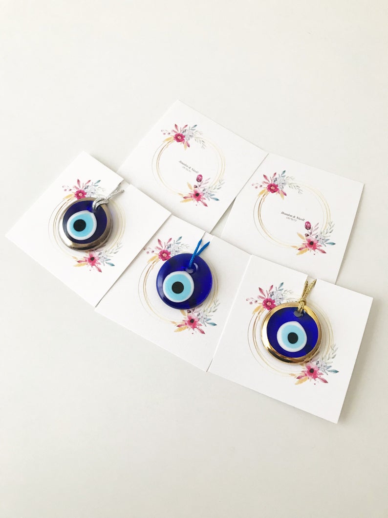 A collection of 10 handmade glass evil eye beads with personalized cards, featuring blue, gold, and silver colors, perfect for wedding favors.