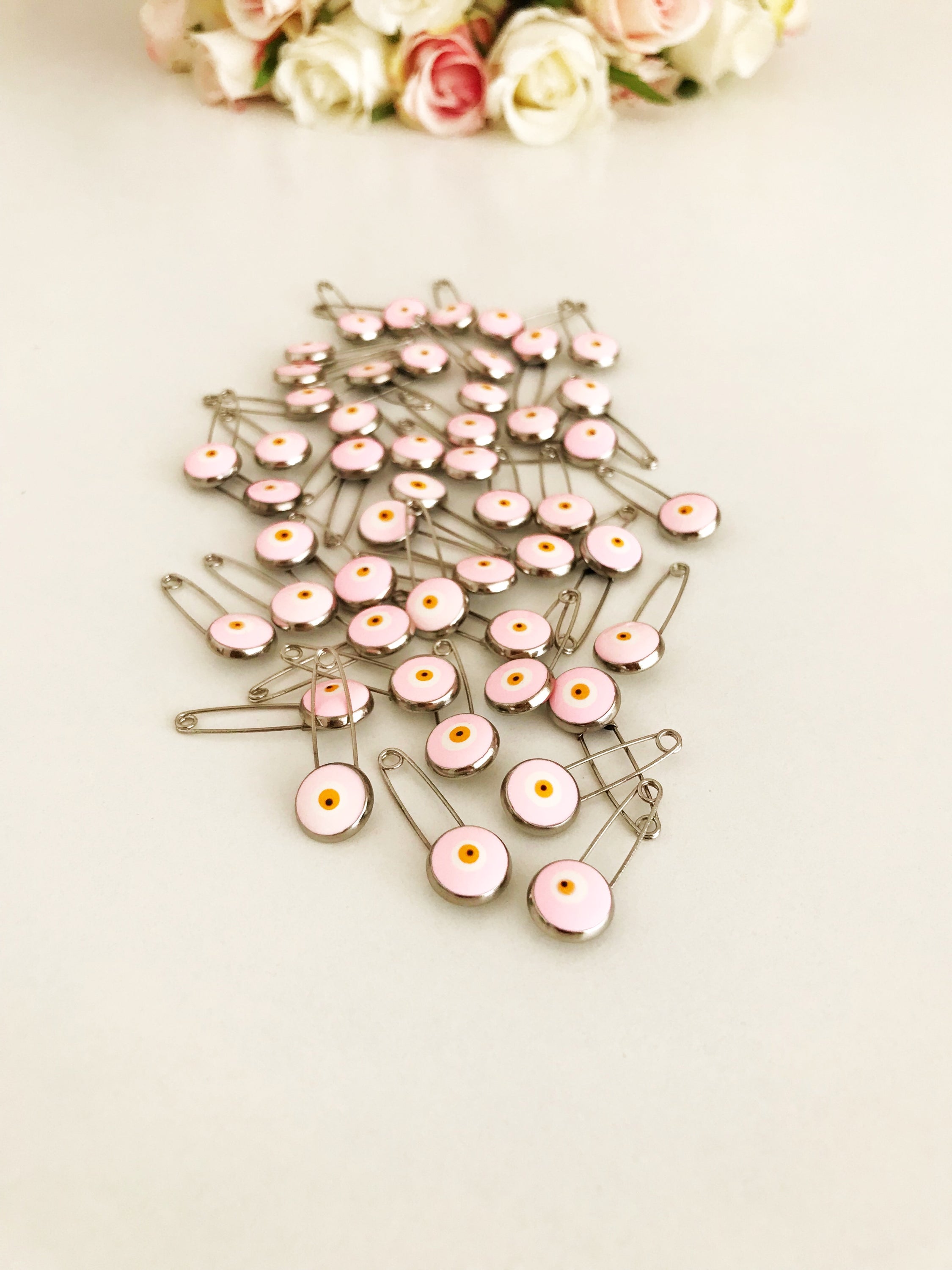 A bulk set of 50 pink evil eye safety pins, featuring a brass construction and an 8mm pink evil eye bead charm, ideal for weddings and baby showers.