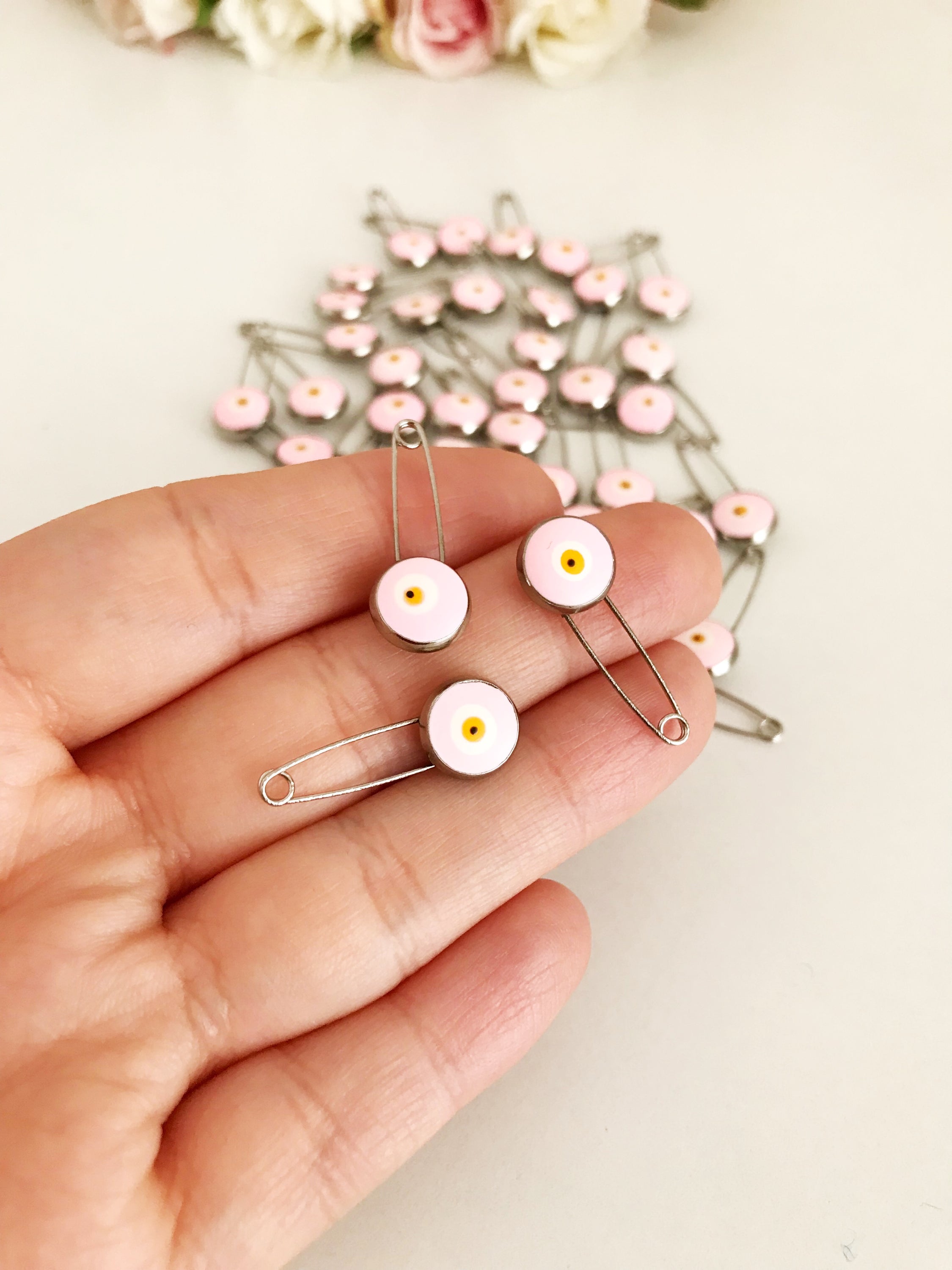 A bulk set of 50 pink evil eye safety pins, featuring a brass construction and an 8mm pink evil eye bead charm, ideal for weddings and baby showers.