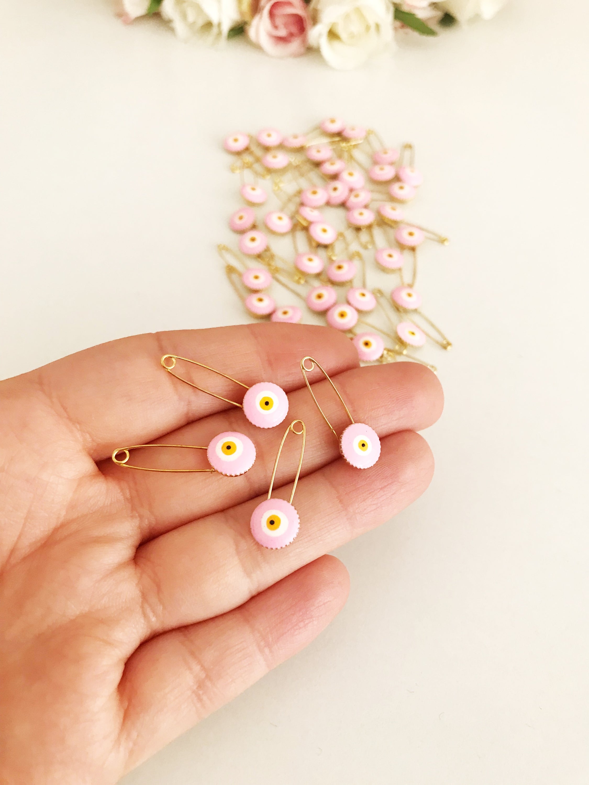 A bulk set of 50 pink evil eye safety pins, featuring a brass construction and an 8mm pink evil eye bead charm, ideal for weddings and baby showers.