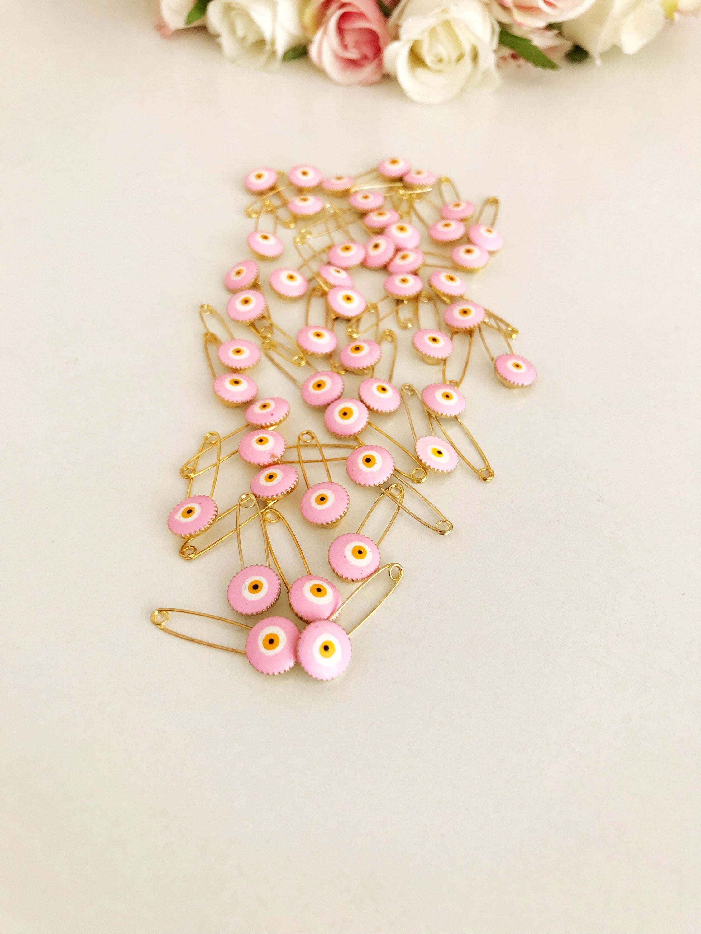 A bulk set of 50 pink evil eye safety pins, featuring a brass construction and an 8mm pink evil eye bead charm, ideal for weddings and baby showers.