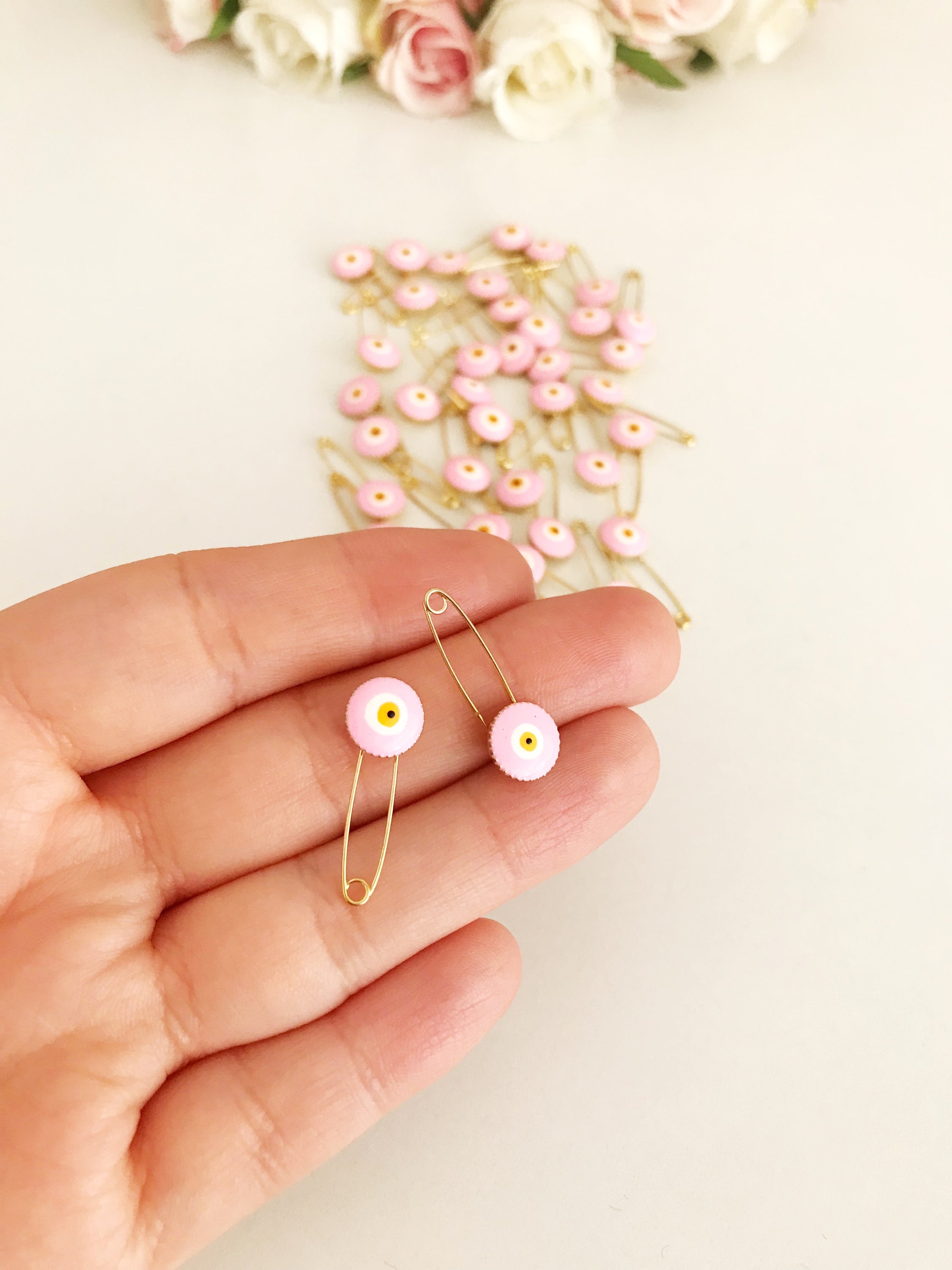 A bulk set of 50 pink evil eye safety pins, featuring a brass construction and an 8mm pink evil eye bead charm, ideal for weddings and baby showers.