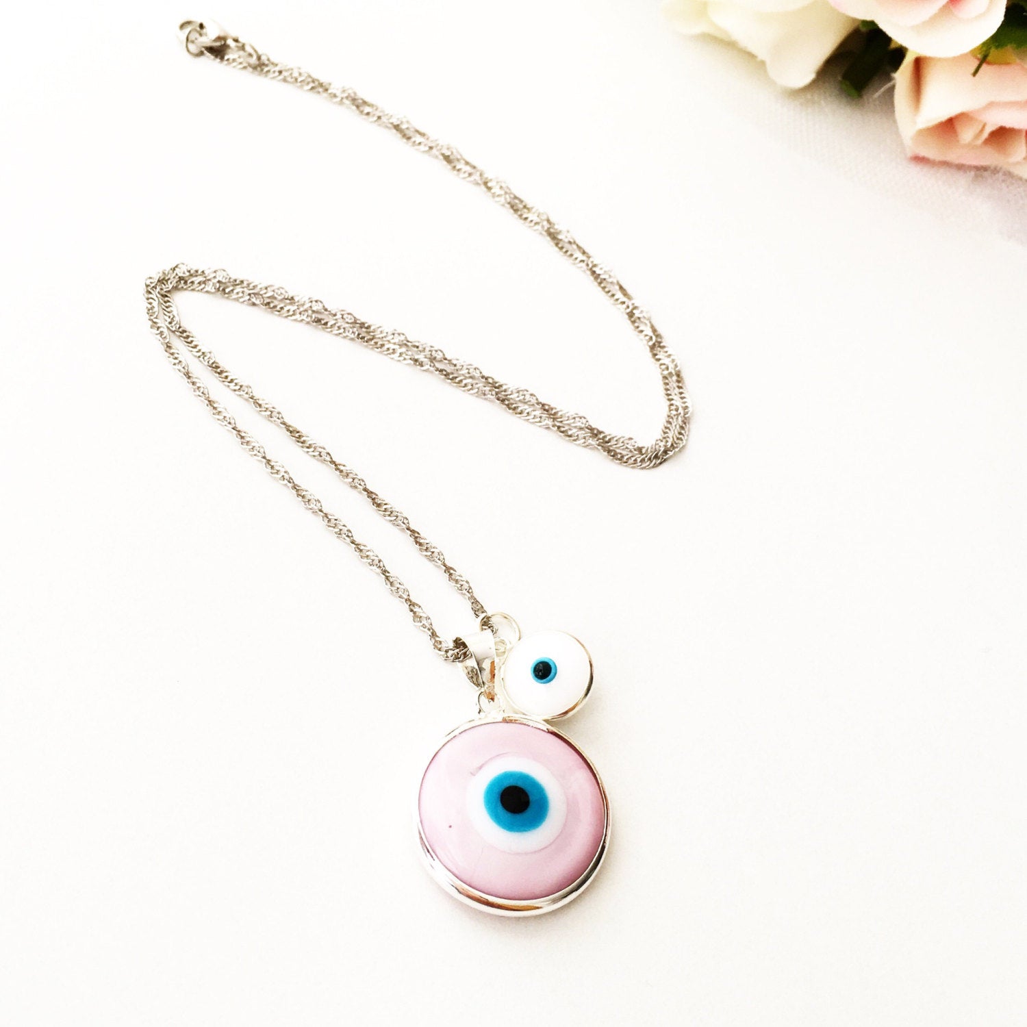 A beautiful Pink Murano Evil Eye Bead Necklace featuring a large pink eye bead and tiny white evil eye beads on a silver plated chain.