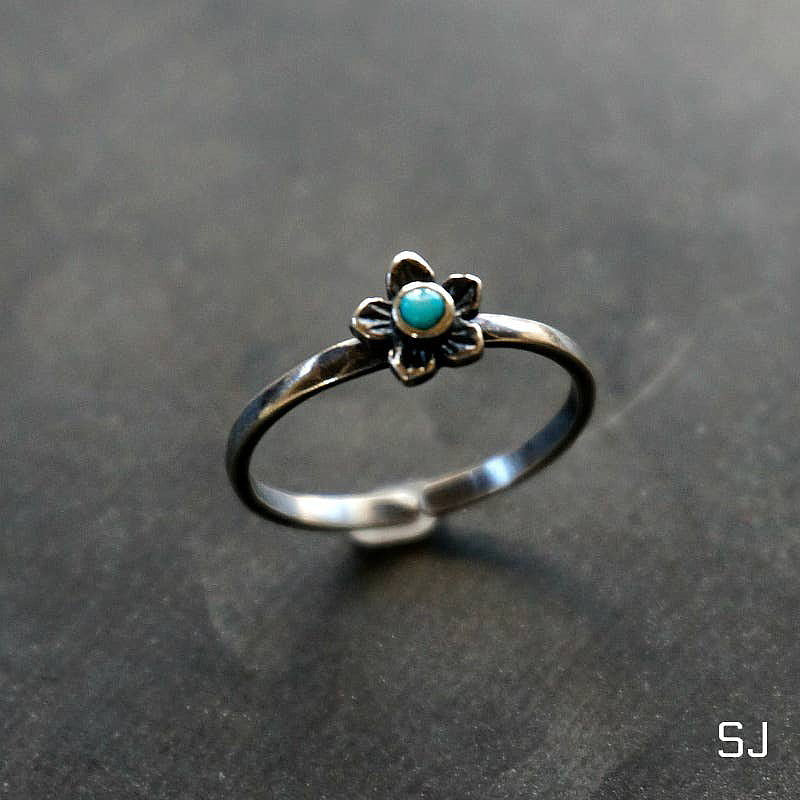 A handcrafted sterling silver ring featuring a plumeria flower design with a genuine turquoise stone, adjustable band for a perfect fit.