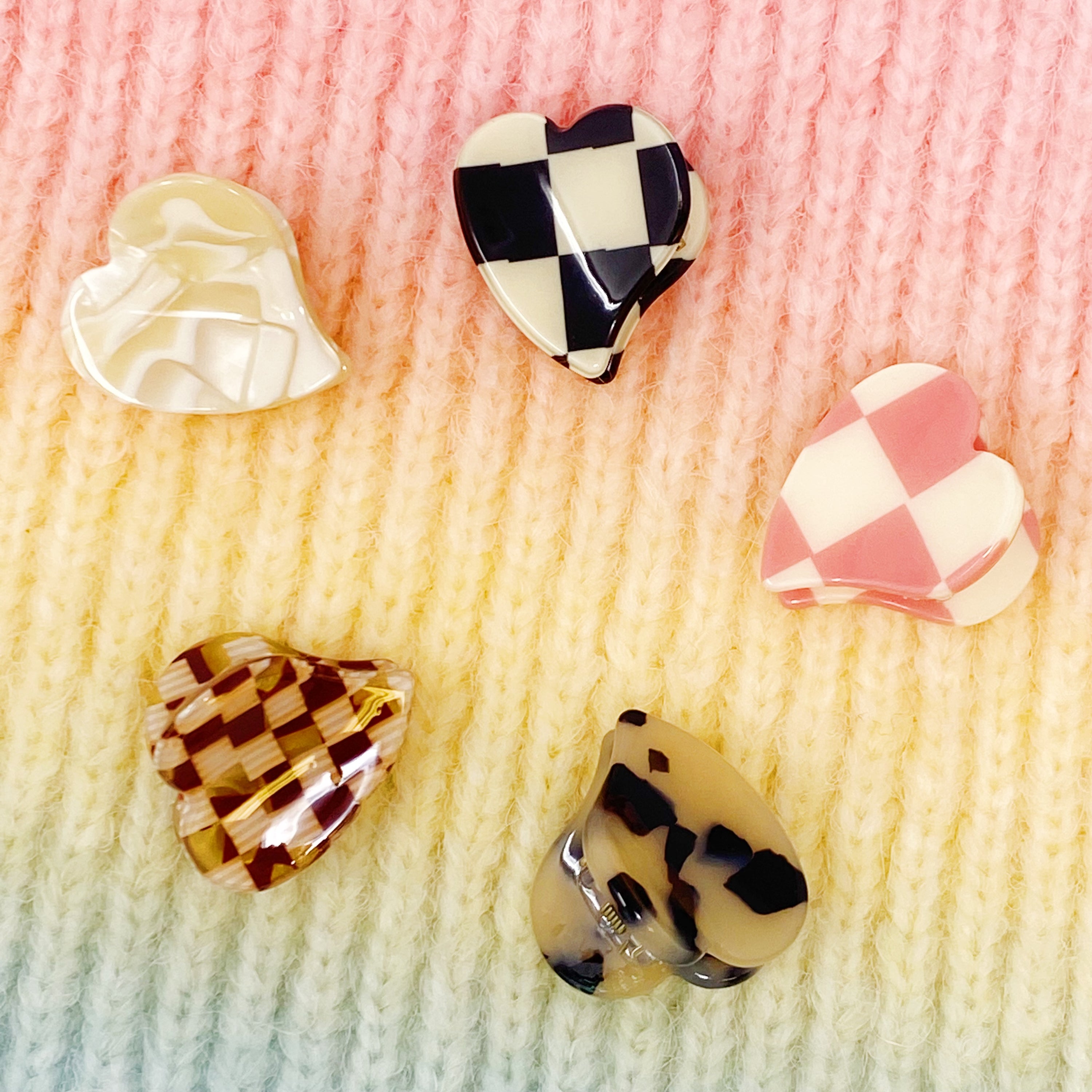 A set of five mini heart-shaped hair claws in various colors, elegantly packaged in a clear cello bag with the Ellison + Young logo.