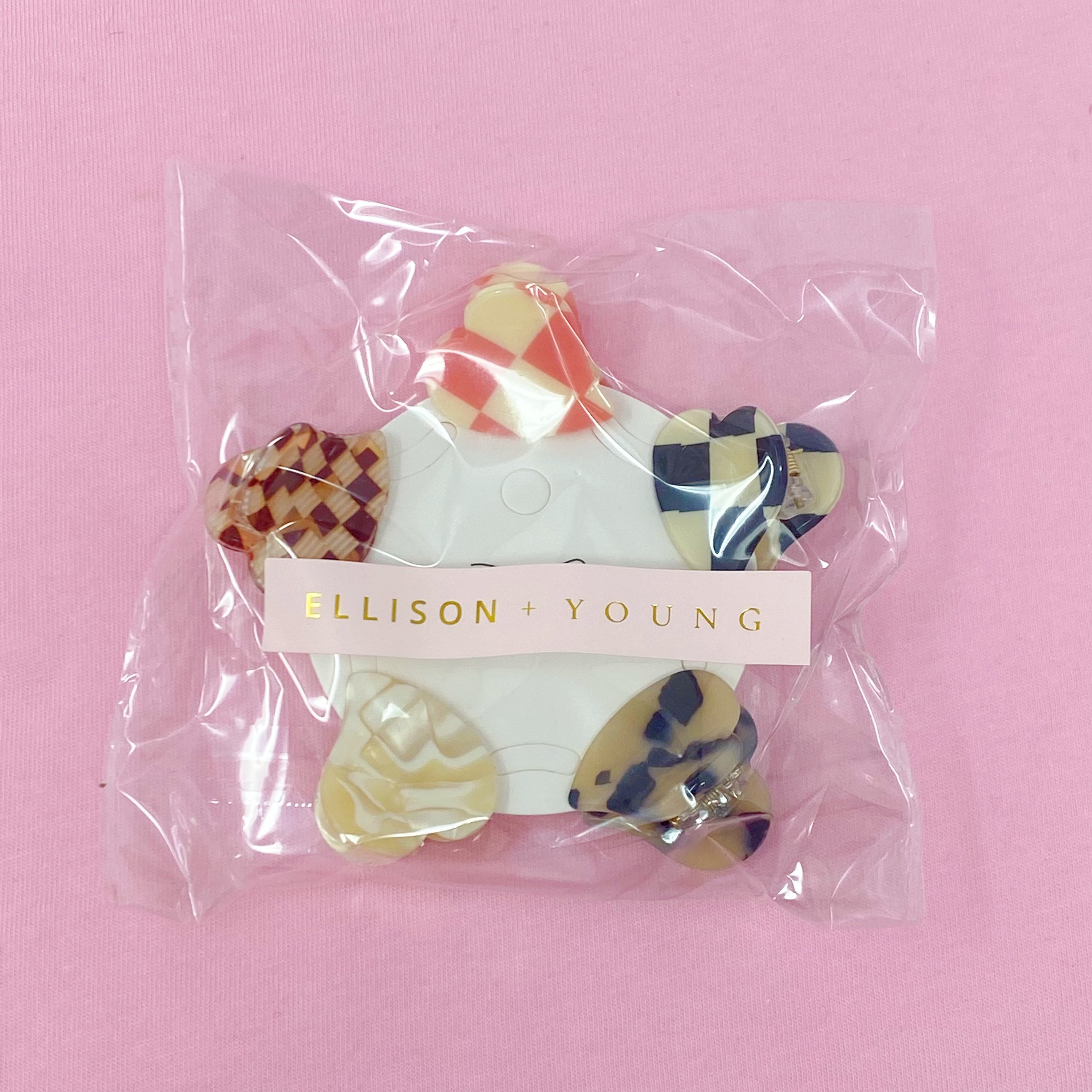 A set of five mini heart-shaped hair claws in various colors, elegantly packaged in a clear cello bag with the Ellison + Young logo.