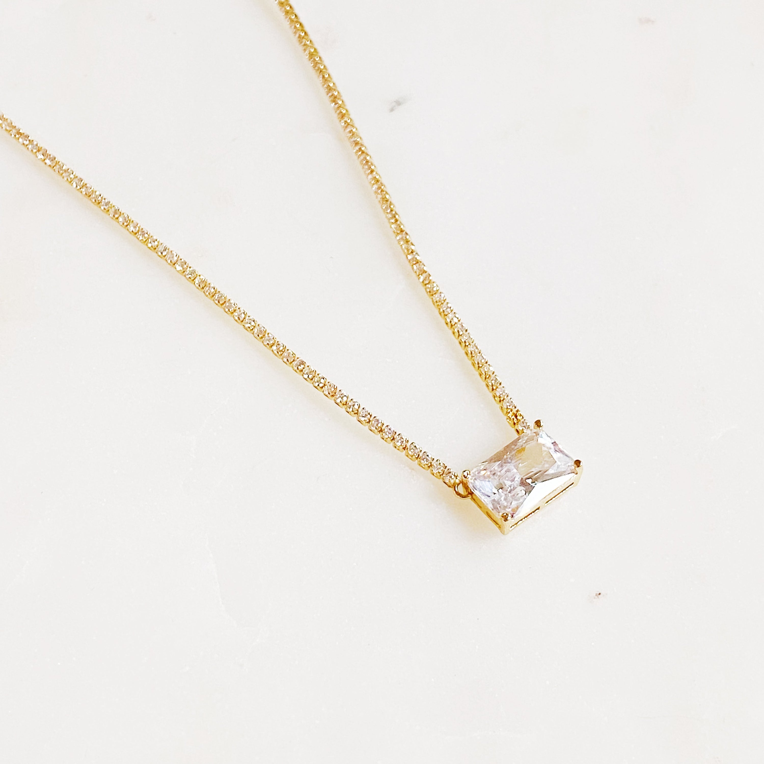 A stunning emerald cut pendant tennis necklace featuring gold-plated brass and sparkling cubic zirconia stones, perfect for elegant occasions.