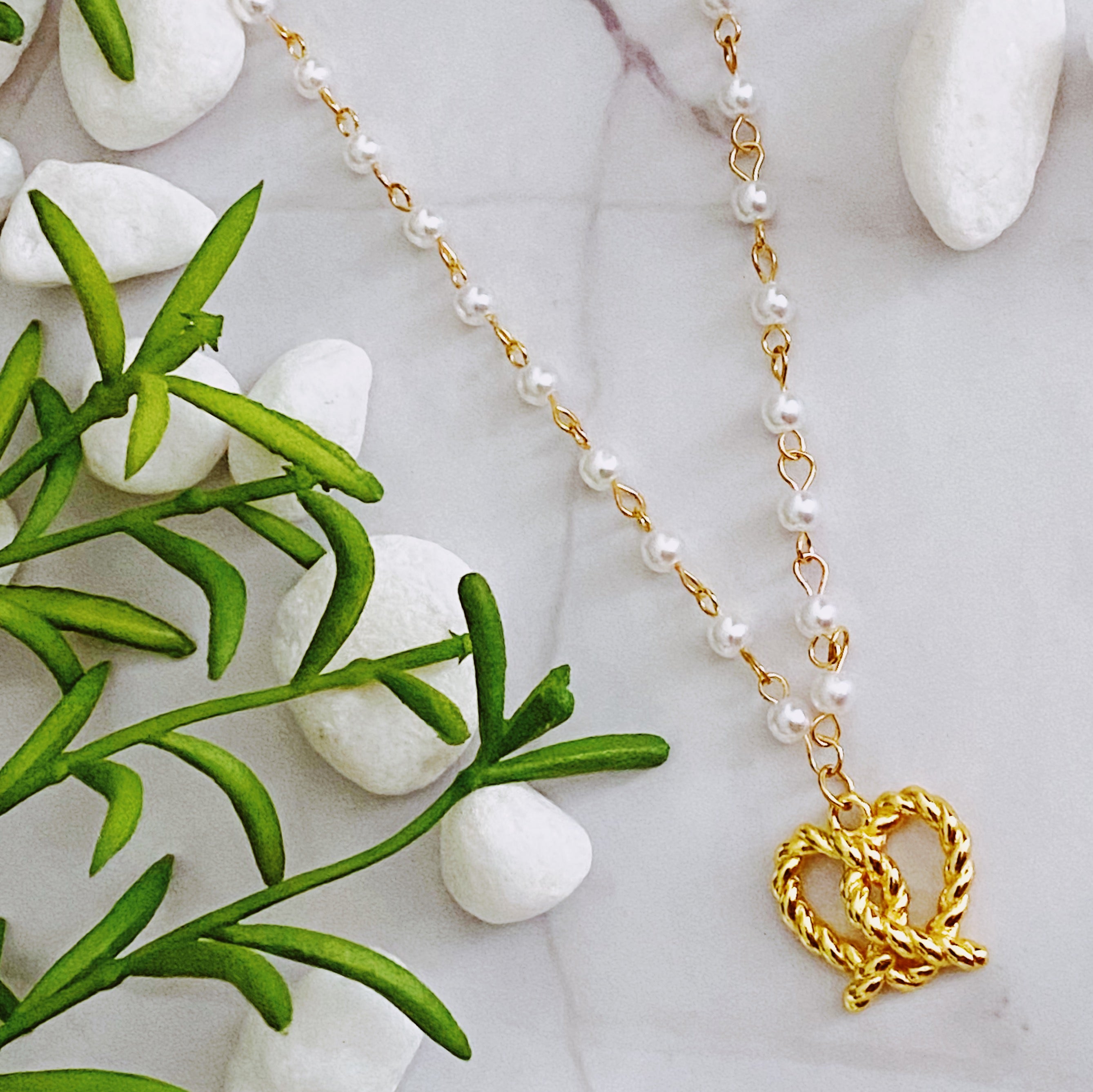 A stylish Pretzel Love Pendant Necklace featuring a heart-shaped pretzel pendant with a pearl mix chain, elegantly crafted in gold plating.