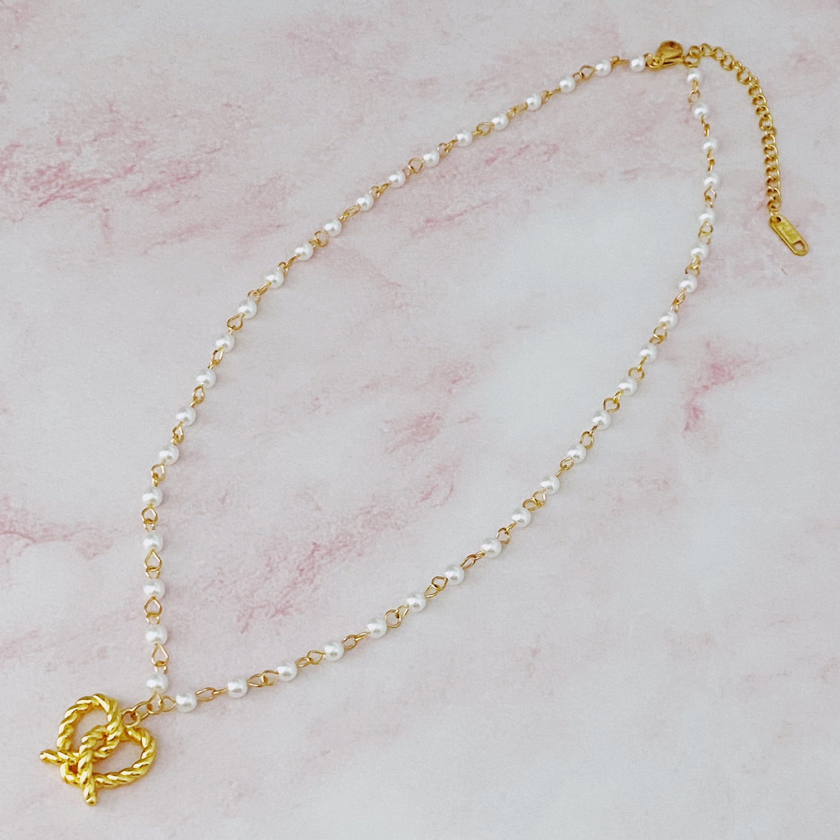 A stylish Pretzel Love Pendant Necklace featuring a heart-shaped pretzel pendant with a pearl mix chain, elegantly crafted in gold plating.