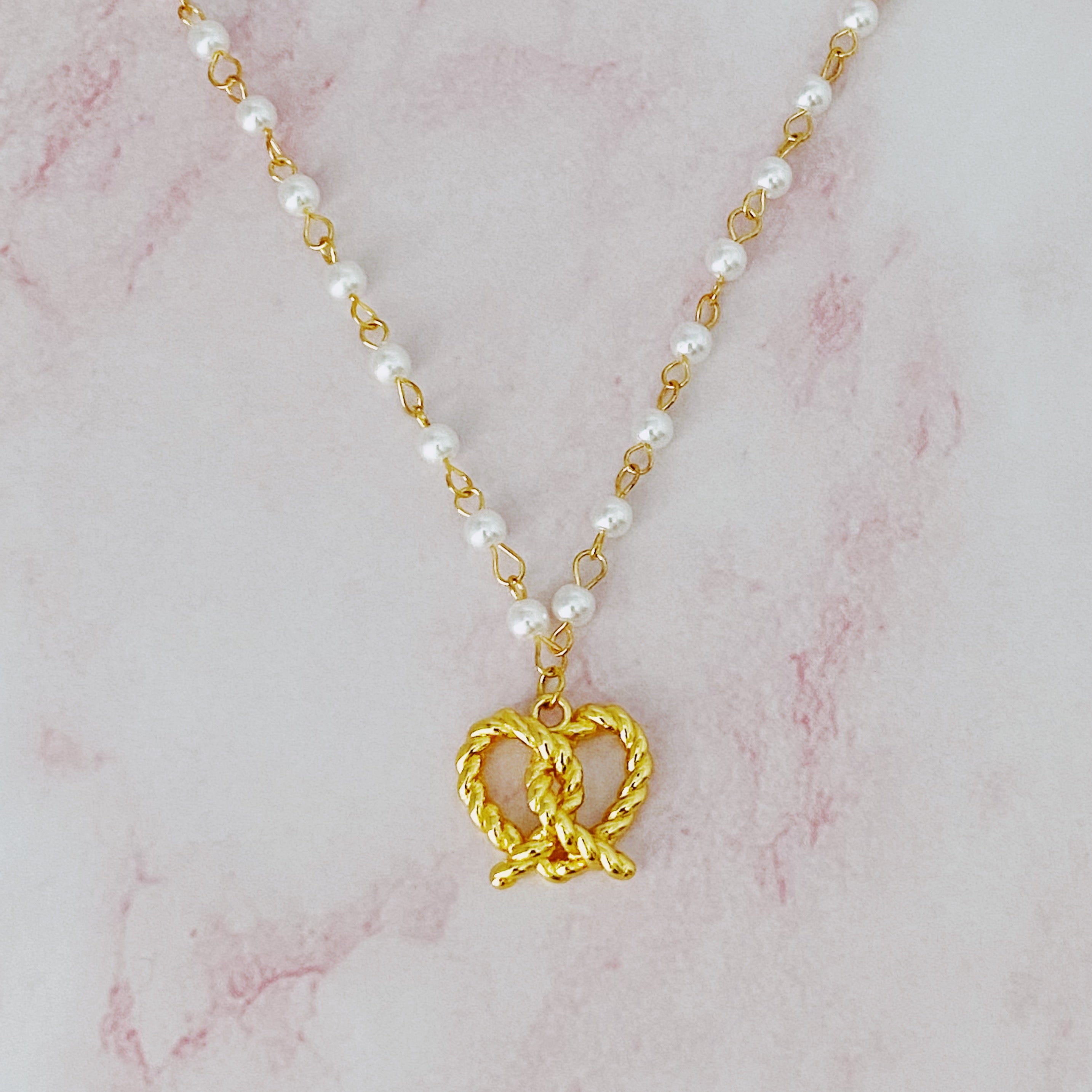 A stylish Pretzel Love Pendant Necklace featuring a heart-shaped pretzel pendant with a pearl mix chain, elegantly crafted in gold plating.