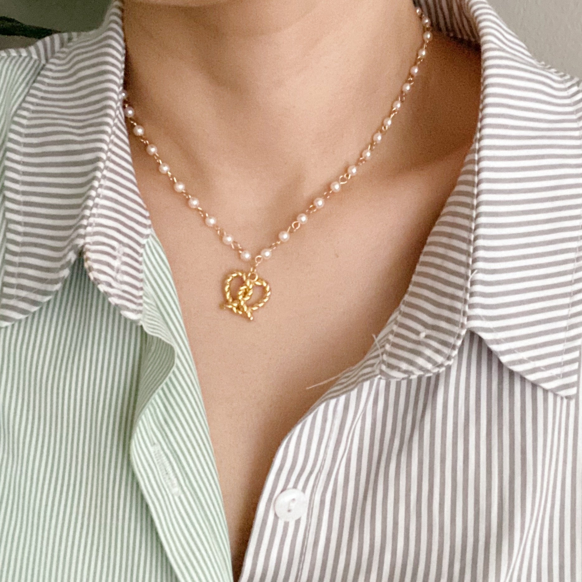 A stylish Pretzel Love Pendant Necklace featuring a heart-shaped pretzel pendant with a pearl mix chain, elegantly crafted in gold plating.