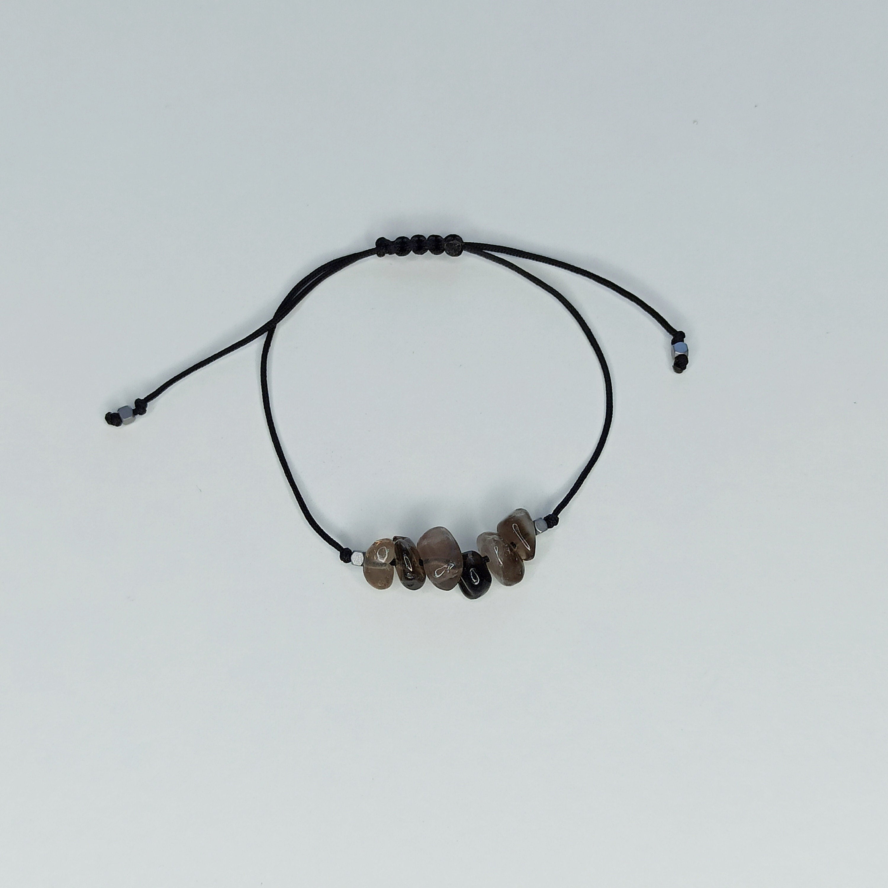 Pulsera de cuarzo ahumado con piedras irregulares sobre fondo blanco, mostrando su diseño ajustable y cordón negro.