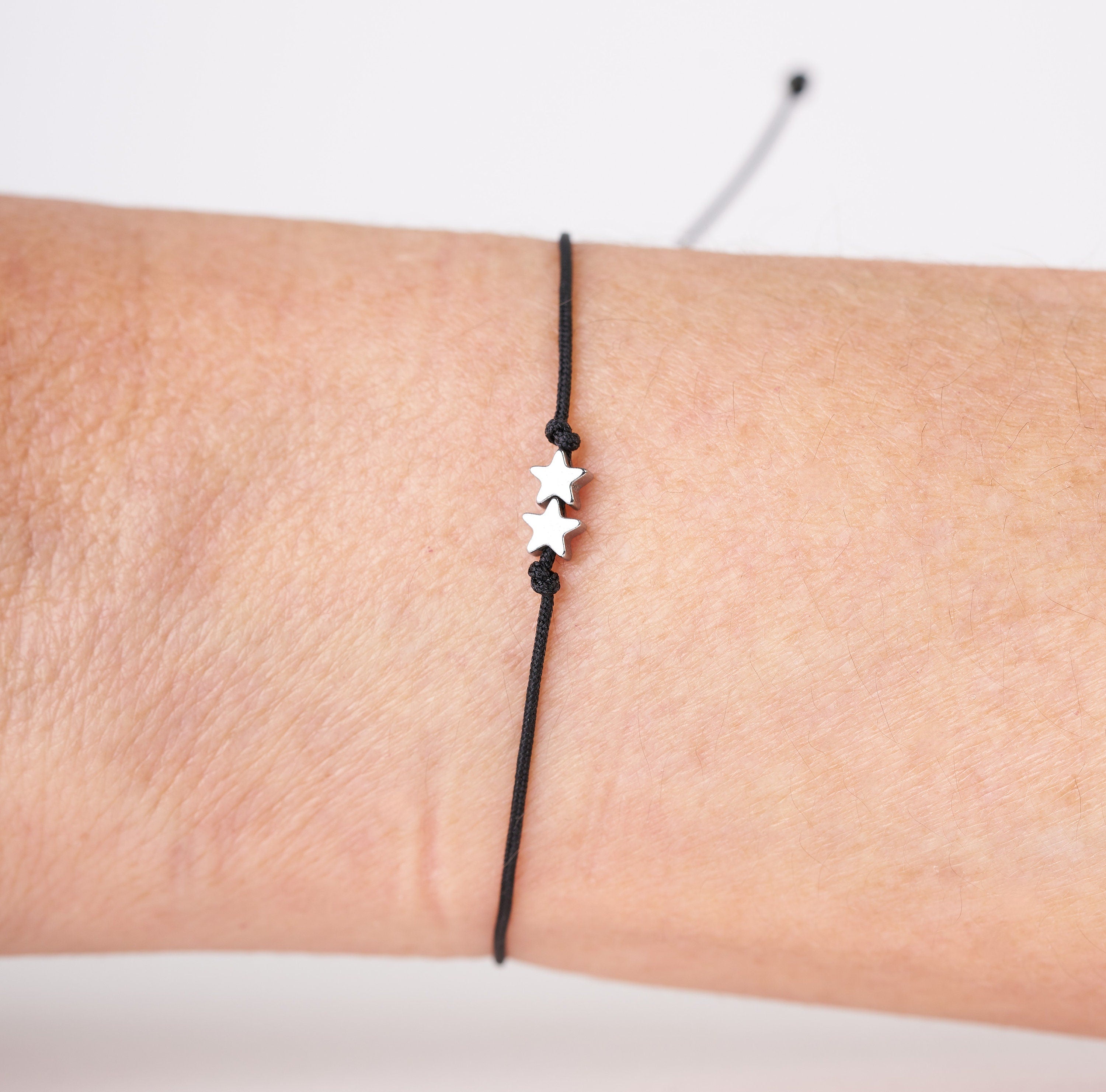 Pulsera con estrellas diminutas de hematita plata y oro, ajustable y hecha a mano, presentada en un pequeño sobre.