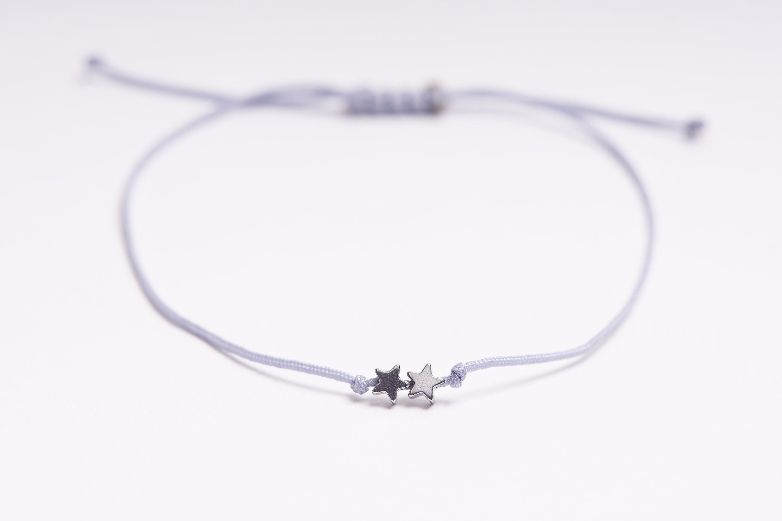 Pulsera con estrellas diminutas de hematita plata y oro, ajustable y hecha a mano, presentada en un pequeño sobre.