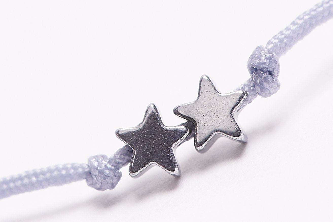 Pulsera con estrellas diminutas de hematita plata y oro, ajustable y hecha a mano, presentada en un pequeño sobre.