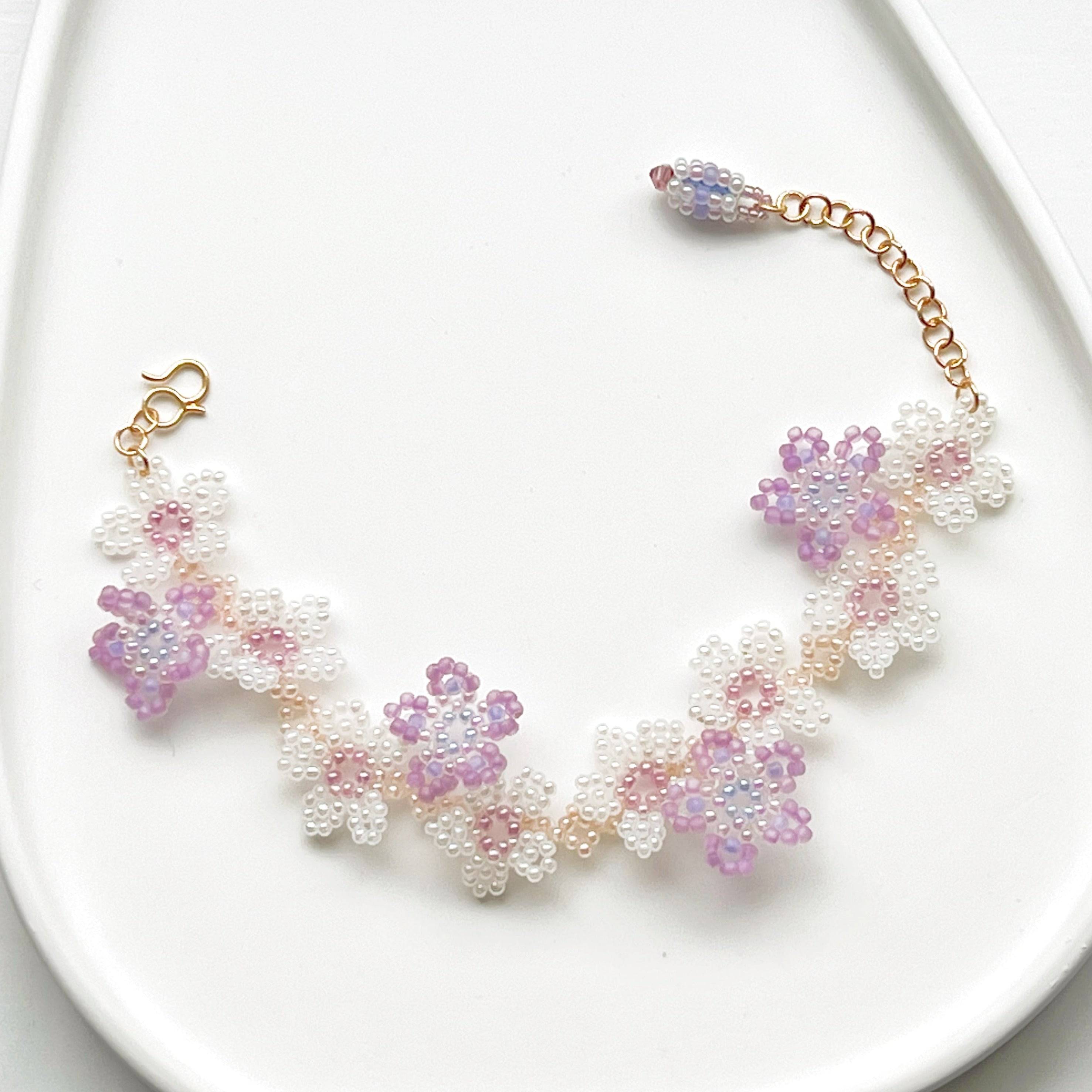 A beautifully handcrafted Purple Cosmos Flower Beaded Bracelet featuring tiny acrylic beads arranged in a floral design, with a gold-plated bronze buckle.