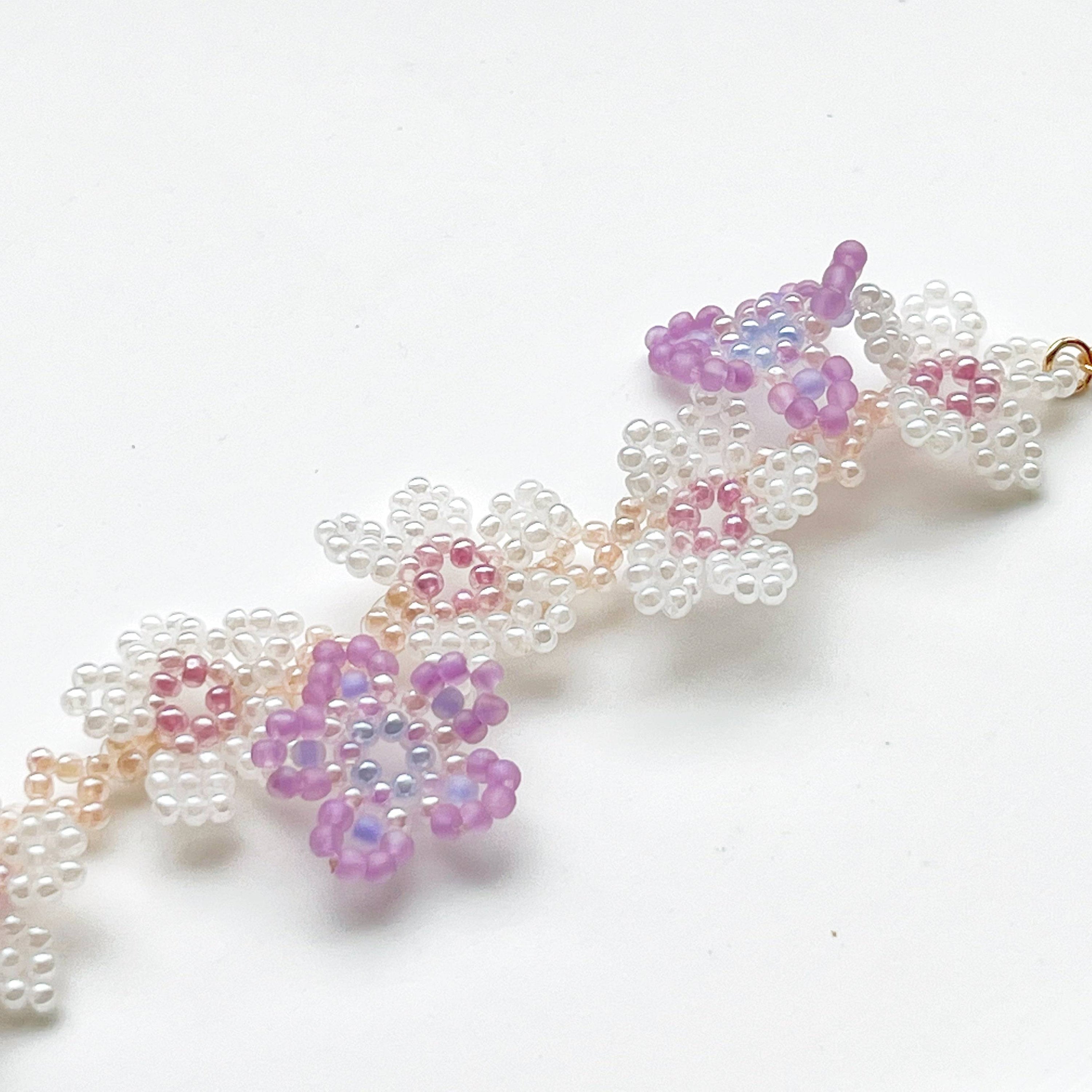 A beautifully handcrafted Purple Cosmos Flower Beaded Bracelet featuring tiny acrylic beads arranged in a floral design, with a gold-plated bronze buckle.