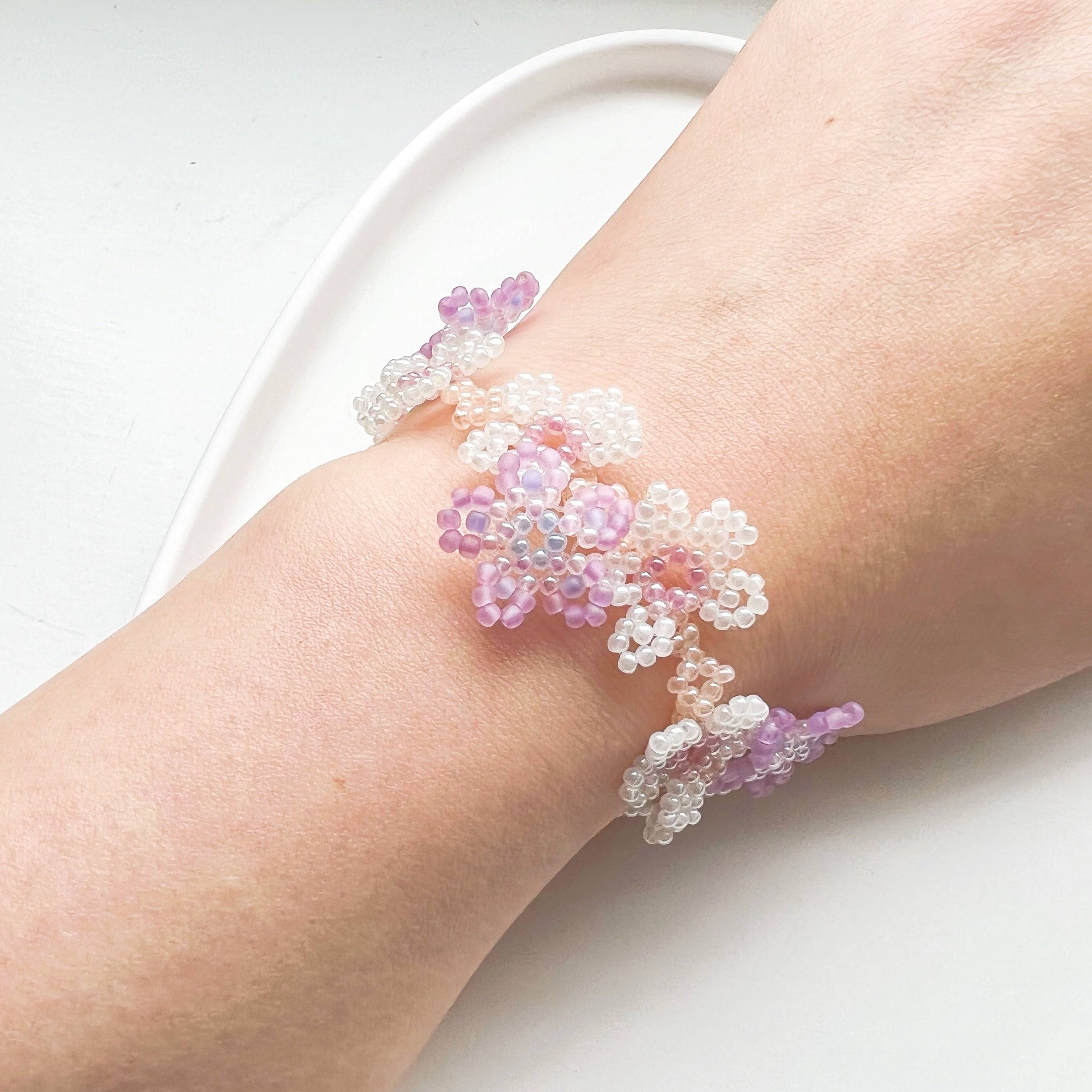 A beautifully handcrafted Purple Cosmos Flower Beaded Bracelet featuring tiny acrylic beads arranged in a floral design, with a gold-plated bronze buckle.