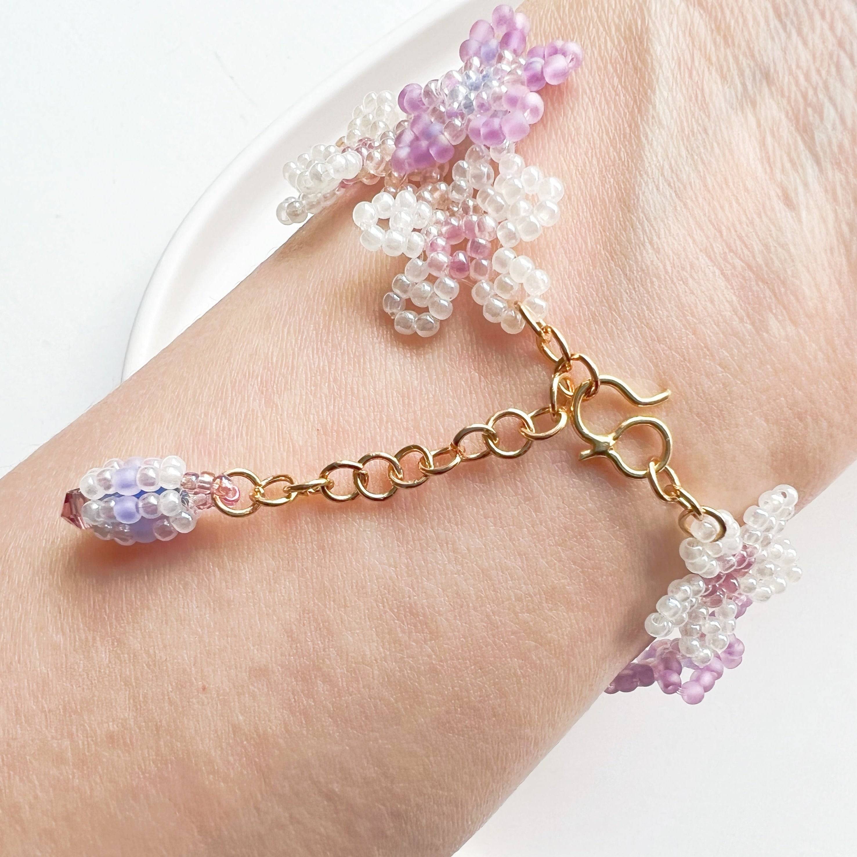 A beautifully handcrafted Purple Cosmos Flower Beaded Bracelet featuring tiny acrylic beads arranged in a floral design, with a gold-plated bronze buckle.