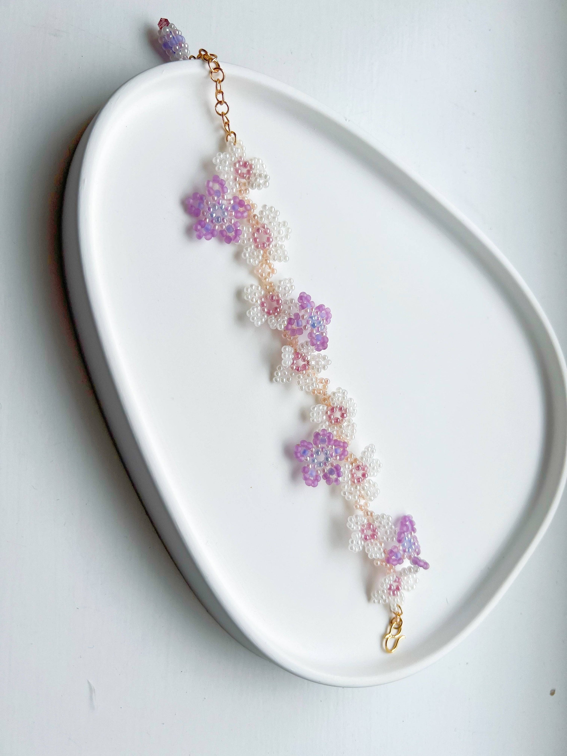 A beautifully handcrafted Purple Cosmos Flower Beaded Bracelet featuring tiny acrylic beads arranged in a floral design, with a gold-plated bronze buckle.