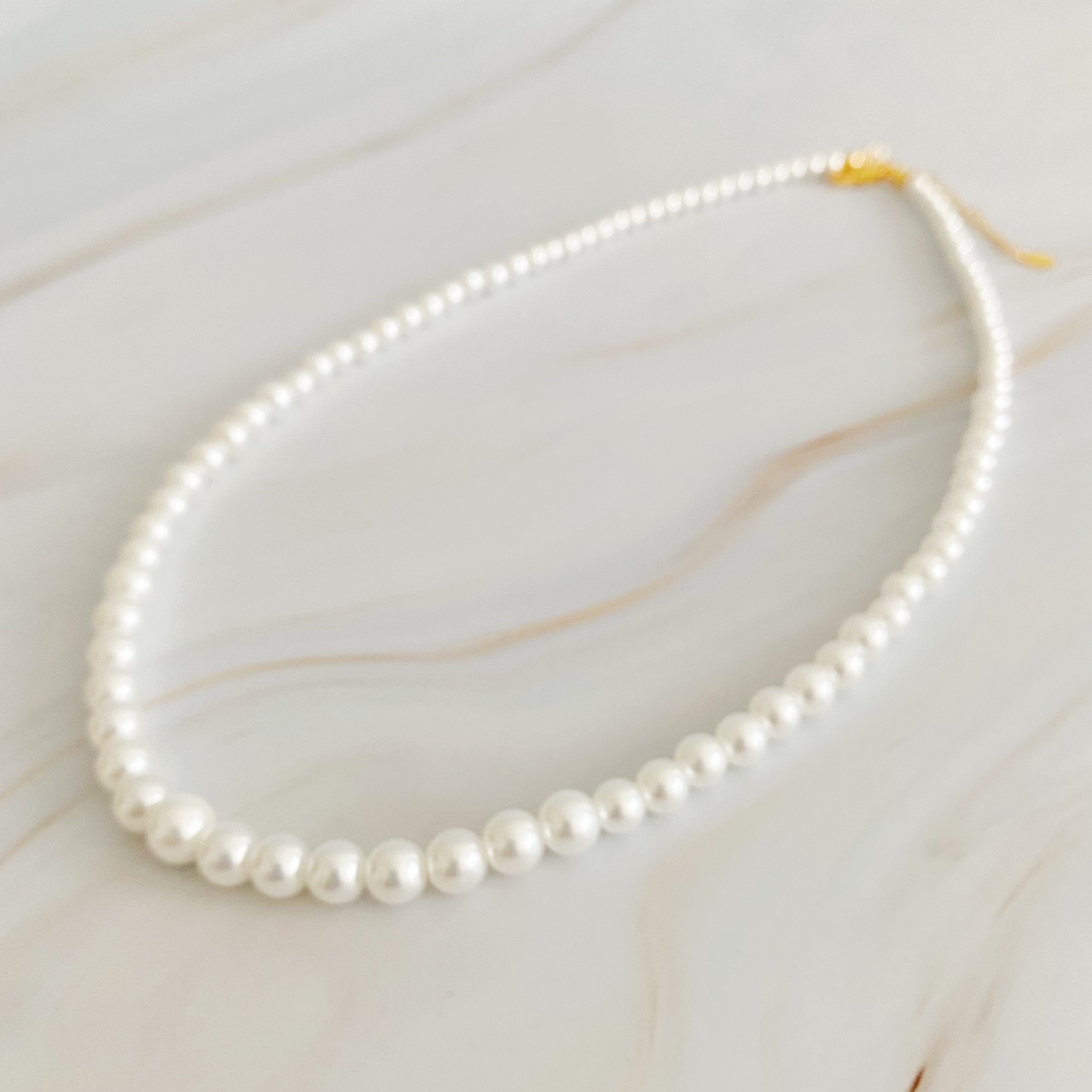 Queen Liz Graduated Pearl Necklace featuring graduated glass pearls from 4mm to 7mm with an 18k gold-plated brass closure.