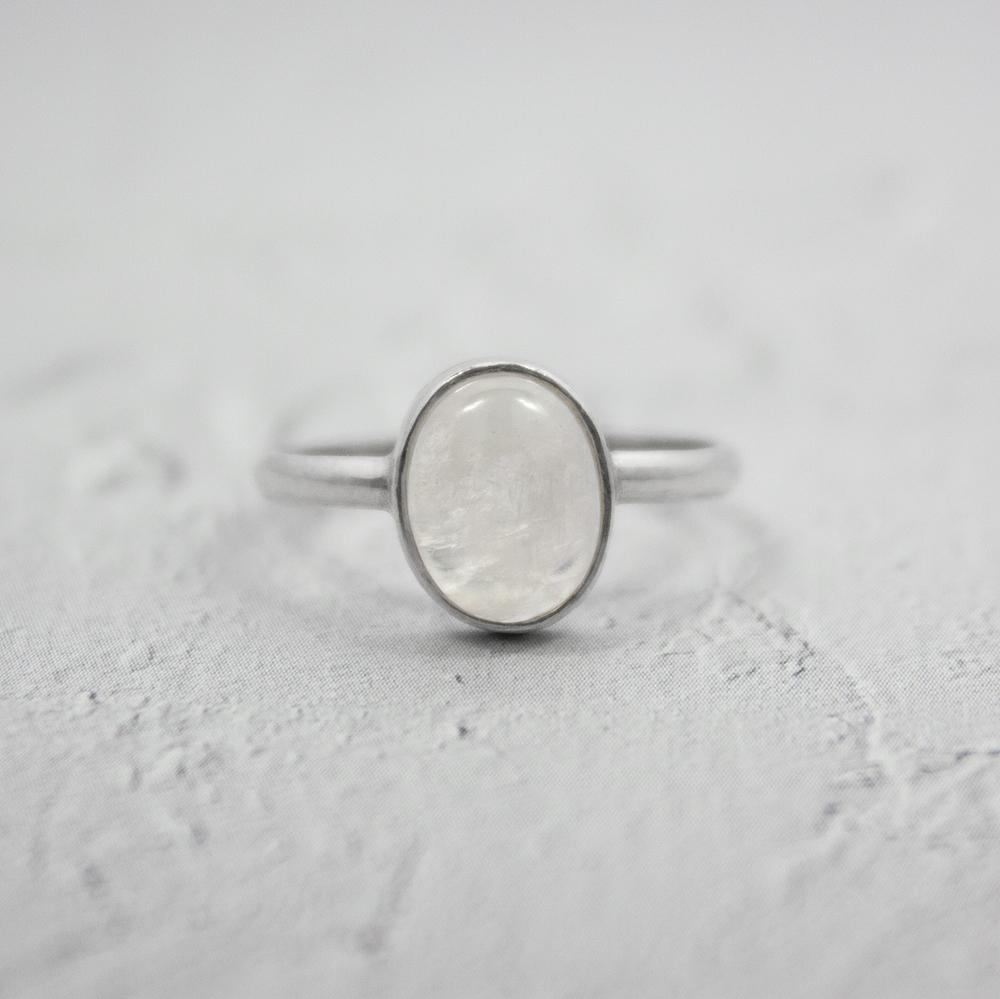 A stunning Rainbow Moonstone Open Bezel Sterling Silver Ring featuring a 9mm x 7mm oval cabochon stone set in a delicate 2mm band.