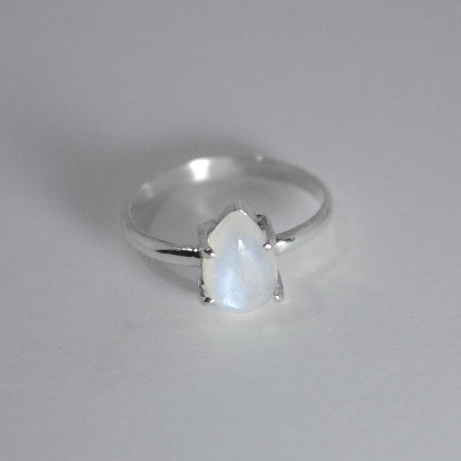 Rainbow Moonstone Pear Claw Sterling Silver Ring featuring a blue flashing pear-shaped moonstone in a claw setting.