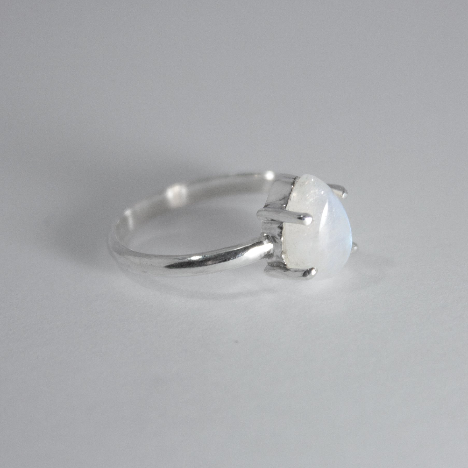 Rainbow Moonstone Pear Claw Sterling Silver Ring featuring a blue flashing pear-shaped moonstone in a claw setting.