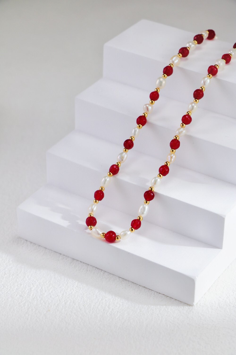 A stunning red beaded necklace featuring baroque freshwater pearls and gold vermeil accents, elegantly displayed on a soft fabric background.