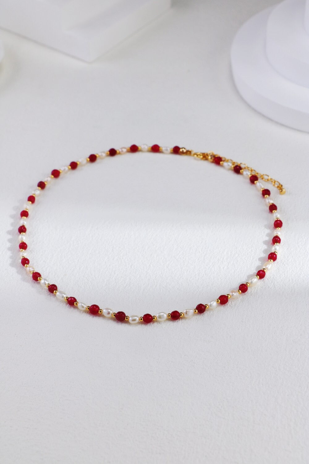 A stunning red beaded necklace featuring baroque freshwater pearls and gold vermeil accents, elegantly displayed on a soft fabric background.