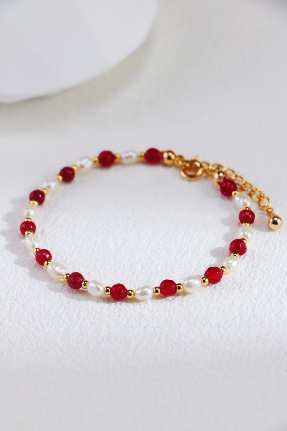 A stunning red beaded necklace featuring baroque freshwater pearls and gold vermeil accents, elegantly displayed on a soft fabric background.