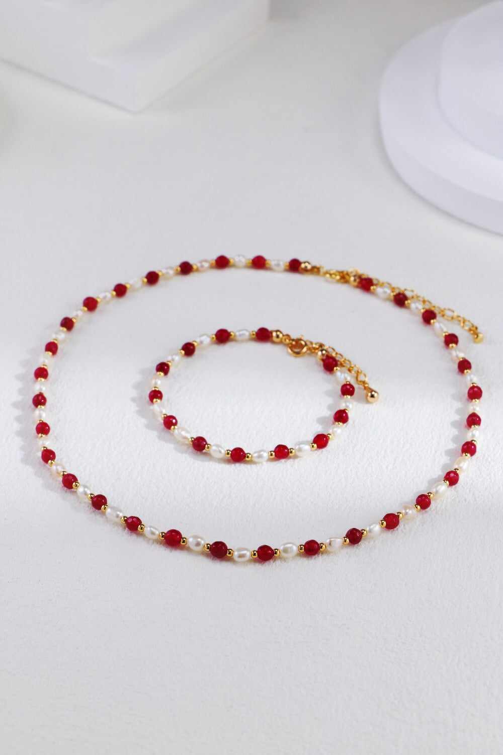 A stunning red beaded necklace featuring baroque freshwater pearls and gold vermeil accents, elegantly displayed on a soft fabric background.