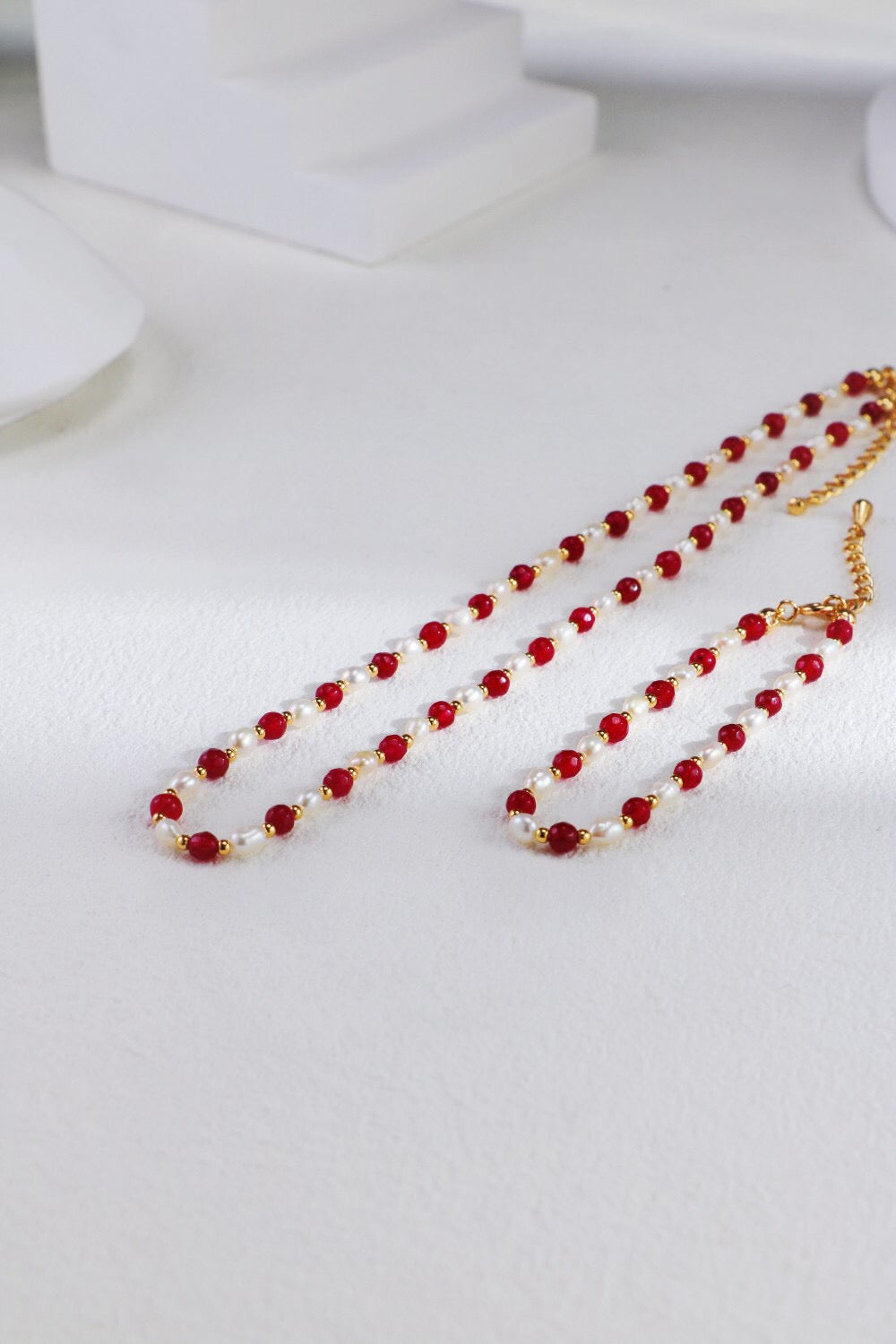 A stunning red beaded necklace featuring baroque freshwater pearls and gold vermeil accents, elegantly displayed on a soft fabric background.