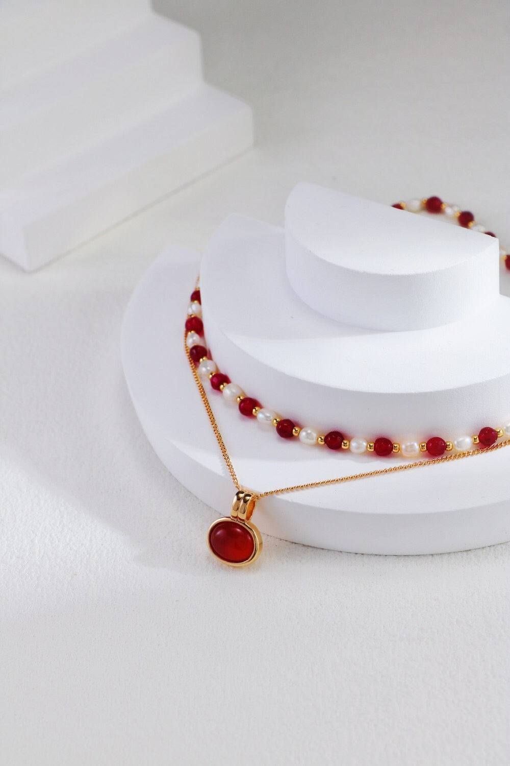 A stunning red beaded necklace featuring baroque freshwater pearls and gold vermeil accents, elegantly displayed on a soft fabric background.