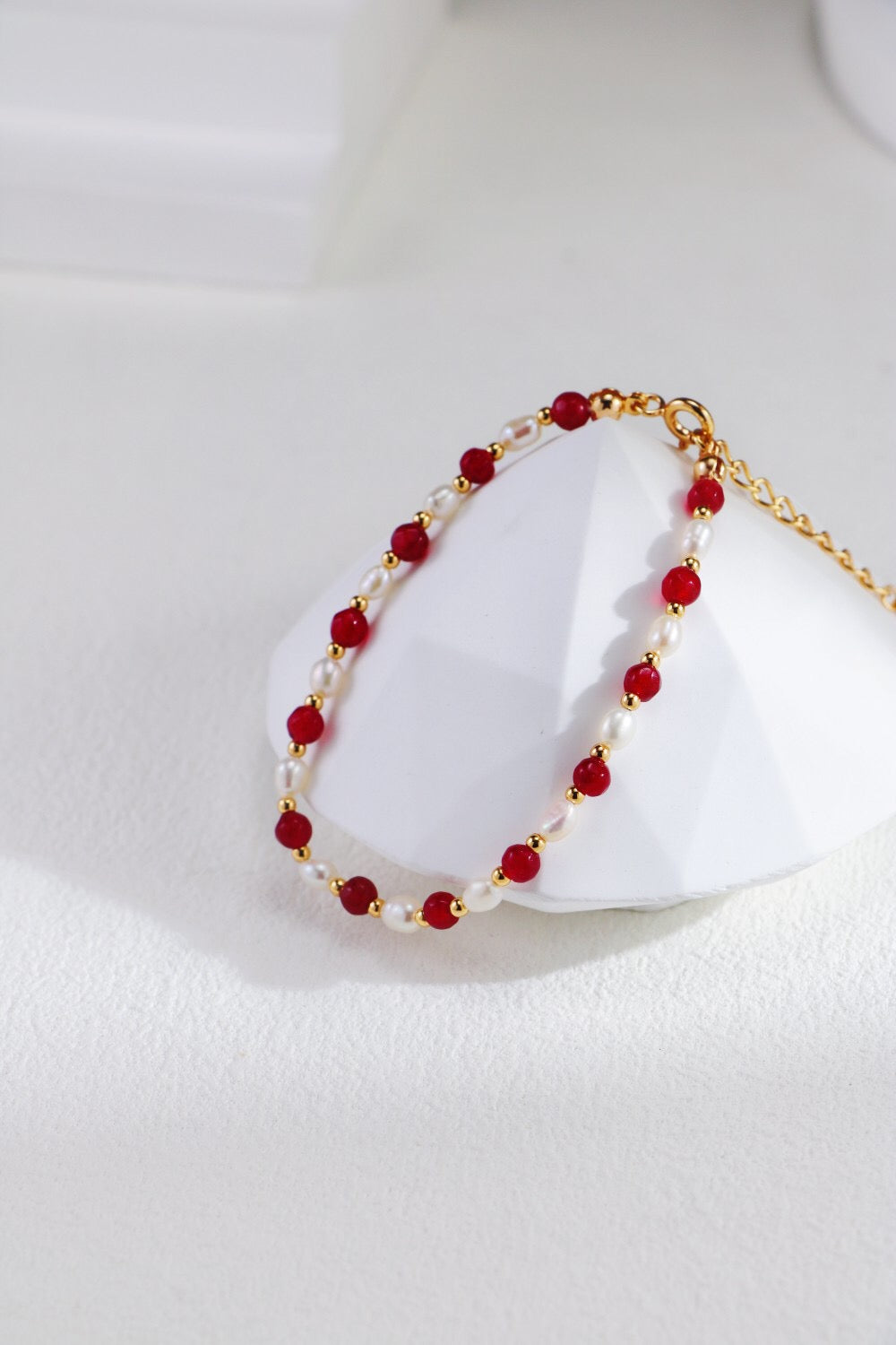 A stunning red beaded necklace featuring baroque freshwater pearls and gold vermeil accents, elegantly displayed on a soft fabric background.