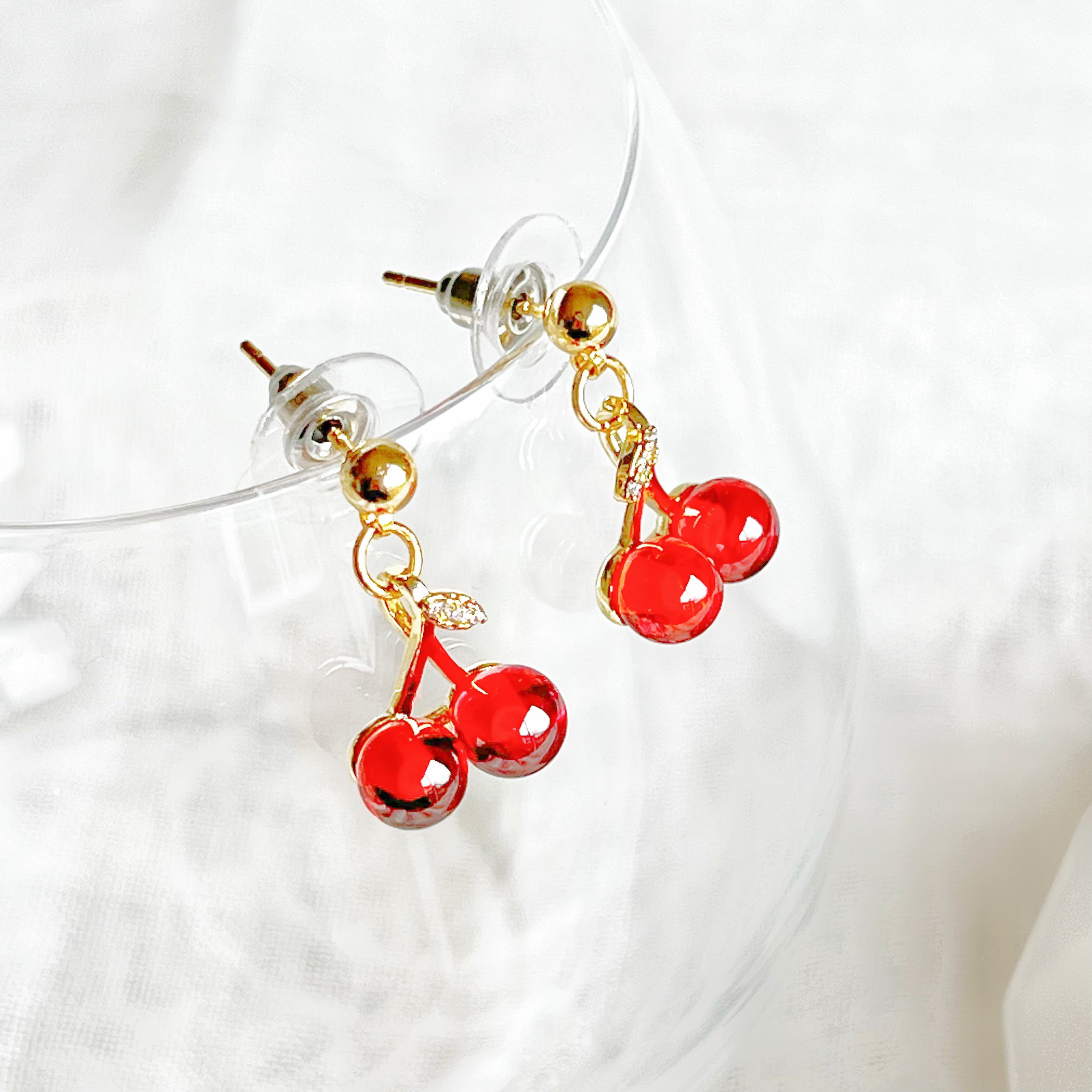 A pair of elegant Red Cherry Mini Drop Earrings featuring red zircon cherries and clear zircon bow ties, set on a gold-plated bronze base.